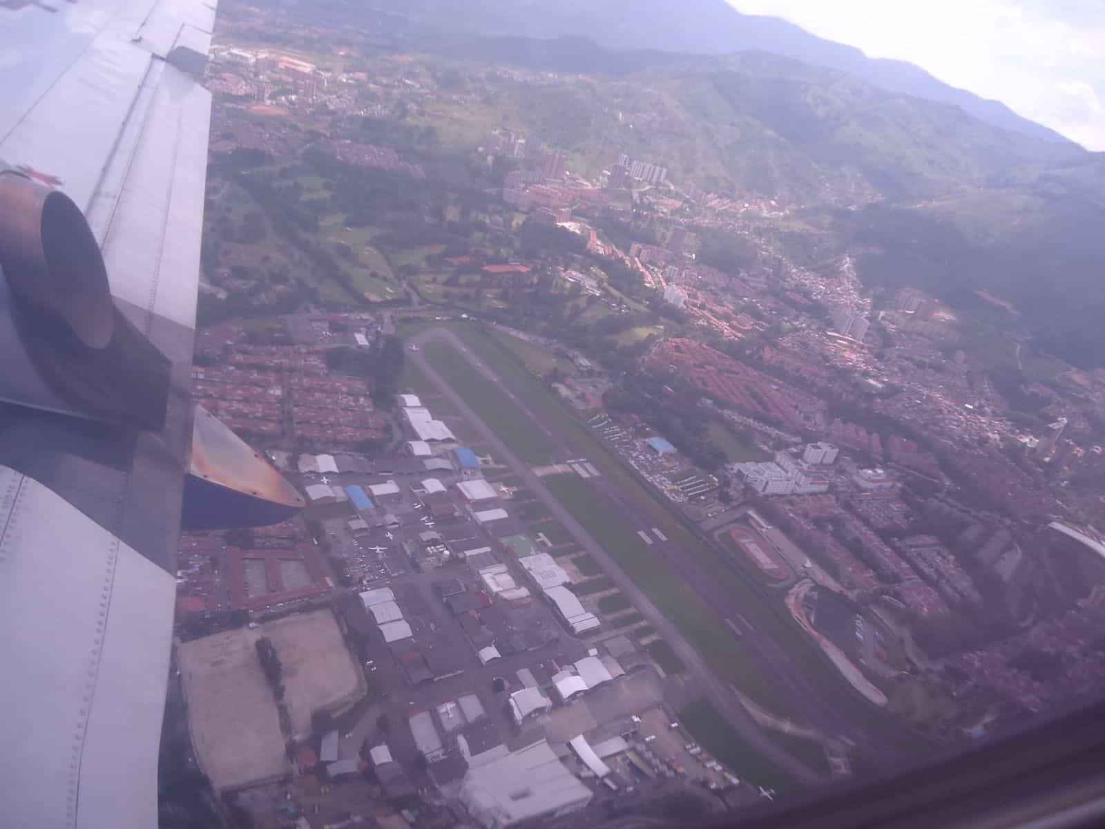 Luftbild des Flughafens Olaya Herrera mitten in Medellín: eine einzige Nord-Süd-Piste, historisches Terminal und Berge des Aburrá-Tals im Hintergrund