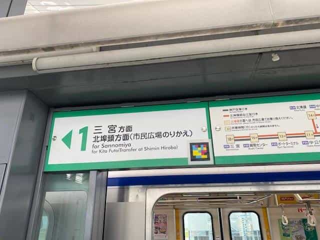 Green platform 1 sign “1 for Sannomiya · for Kita Futo (Transfer at Shimin Hiroba)” with NaviLens tag at its lower right corner; below, open Port Liner platform-screen doors