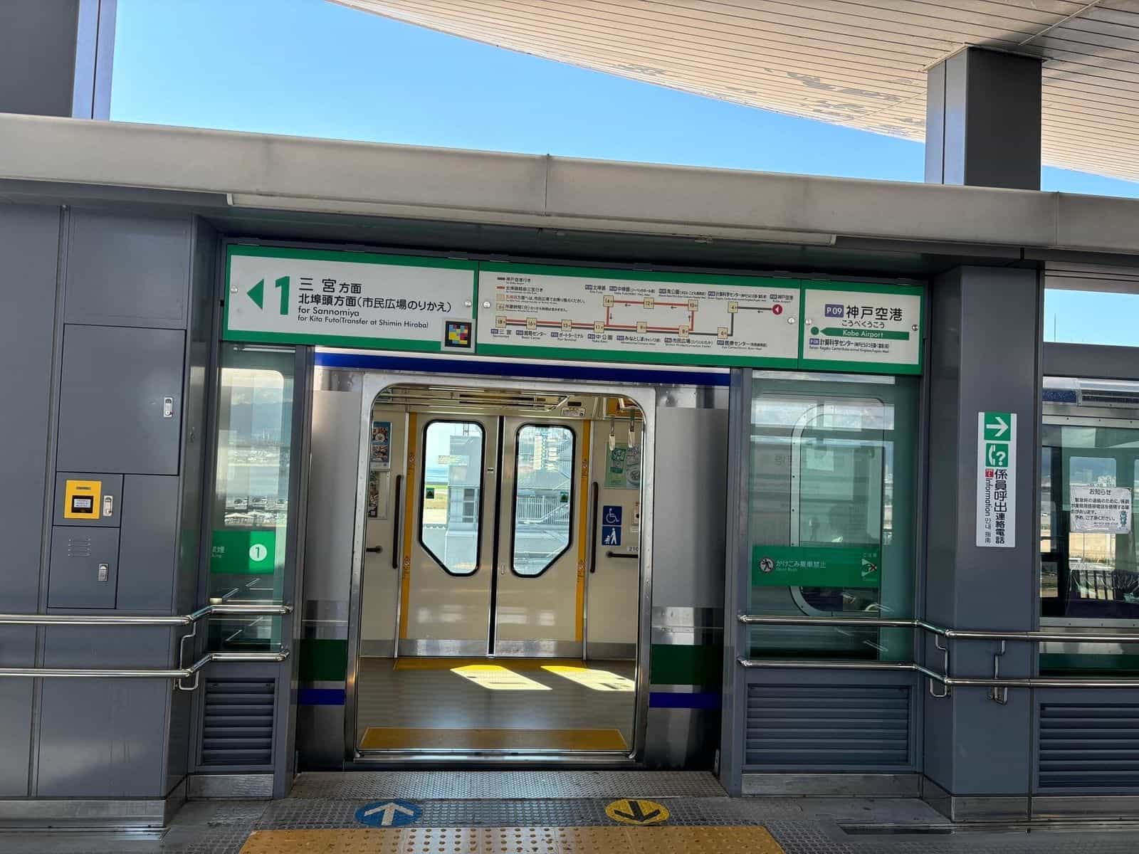 Platform 1 of station P09 Kobe Airport (Port Liner) with a train standing, doors open towards Sannomiya; above the door, green platform sign with NaviLens tag and, on the right, line map with every stop (P01 Sannomiya → P09 Kobe Airport)
