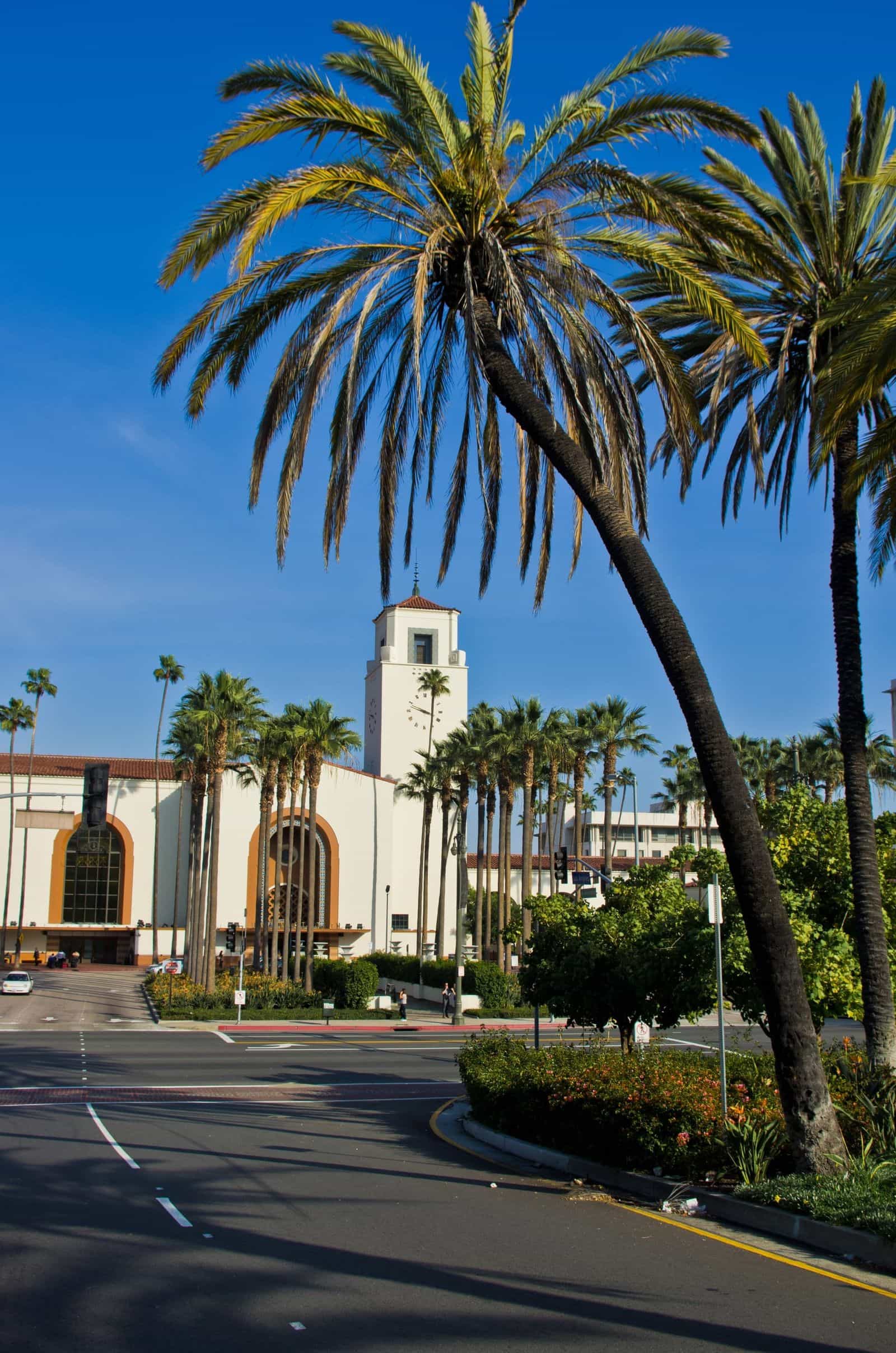 Banchine della Union Station: treni di Amtrak e Metrolink in sosta sotto pensiline storiche in ferro e vetro, con passerella pedonale sopraelevata di collegamento alla rete metropolitana