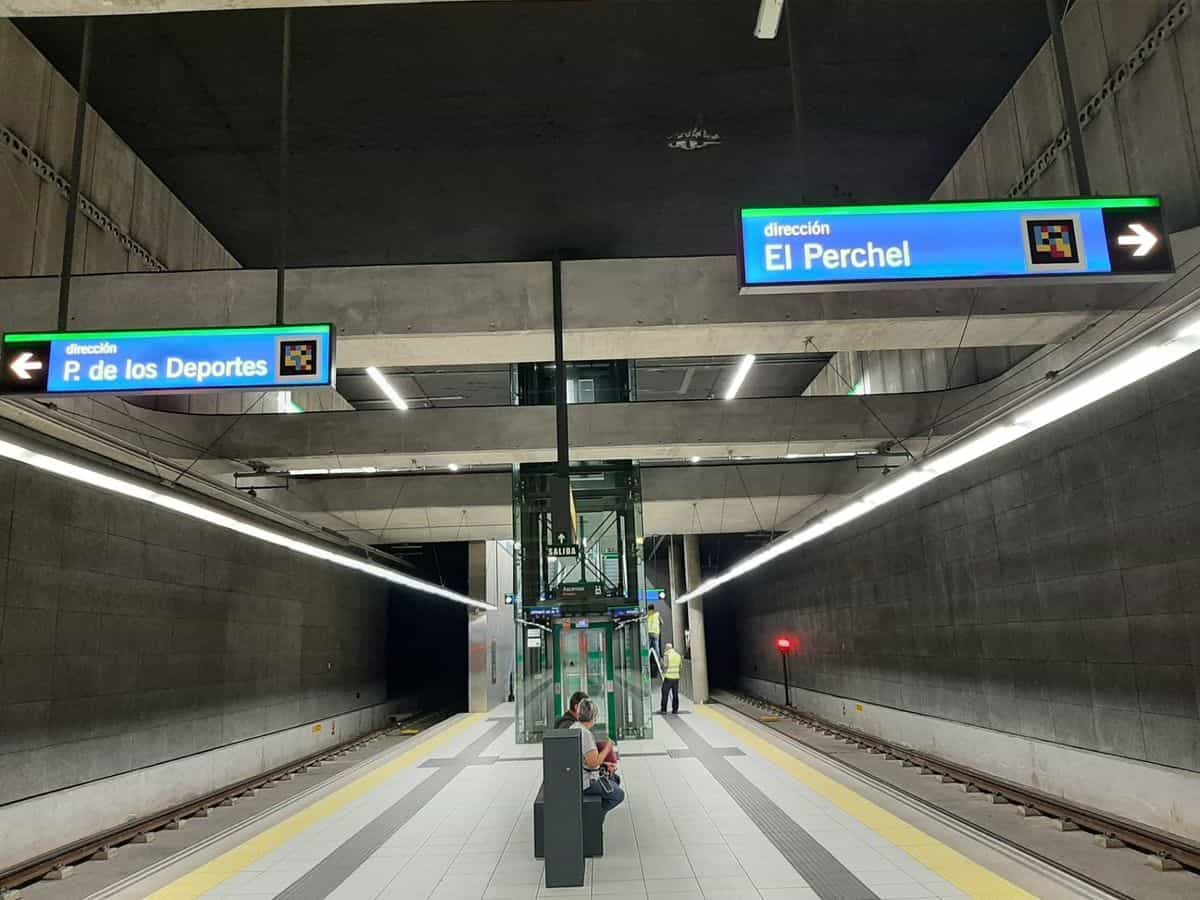 Andén central subterráneo del Metro de Málaga con dos carteles luminosos azules «dirección P. de los Deportes» y «dirección El Perchel» con códigos NaviLens