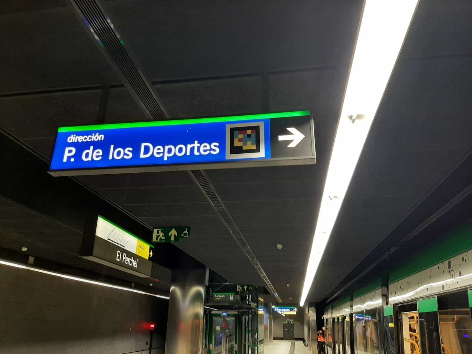 Cartello luminoso azzurro «dirección P. de los Deportes» con codice NaviLens; sotto, il treno fermo con le fasce verdi