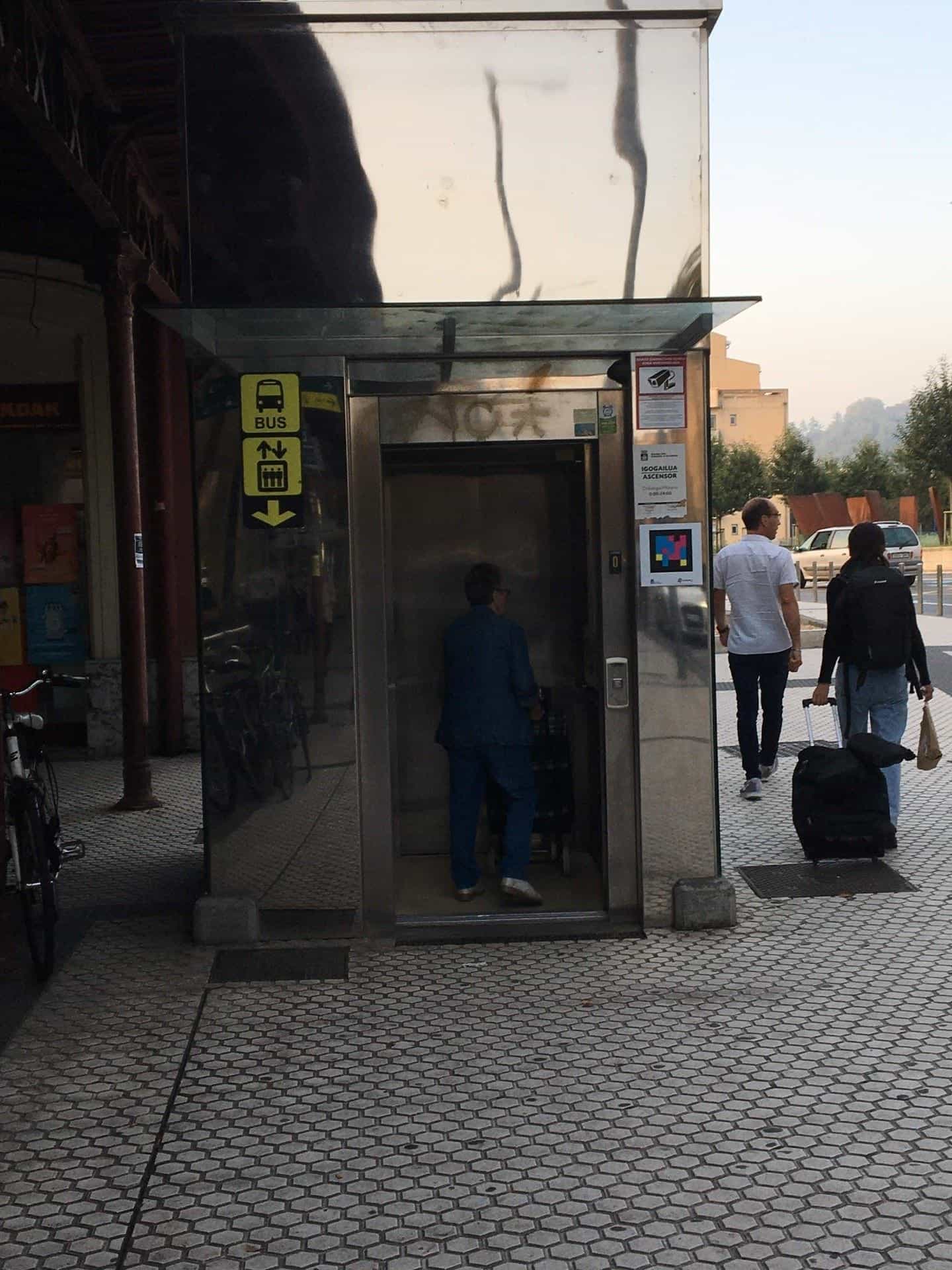Cabina dell’ascensore esterno con cartello BUS e codice NaviLens accanto all’orario Igogailua / Ascensore 6:00-24:00