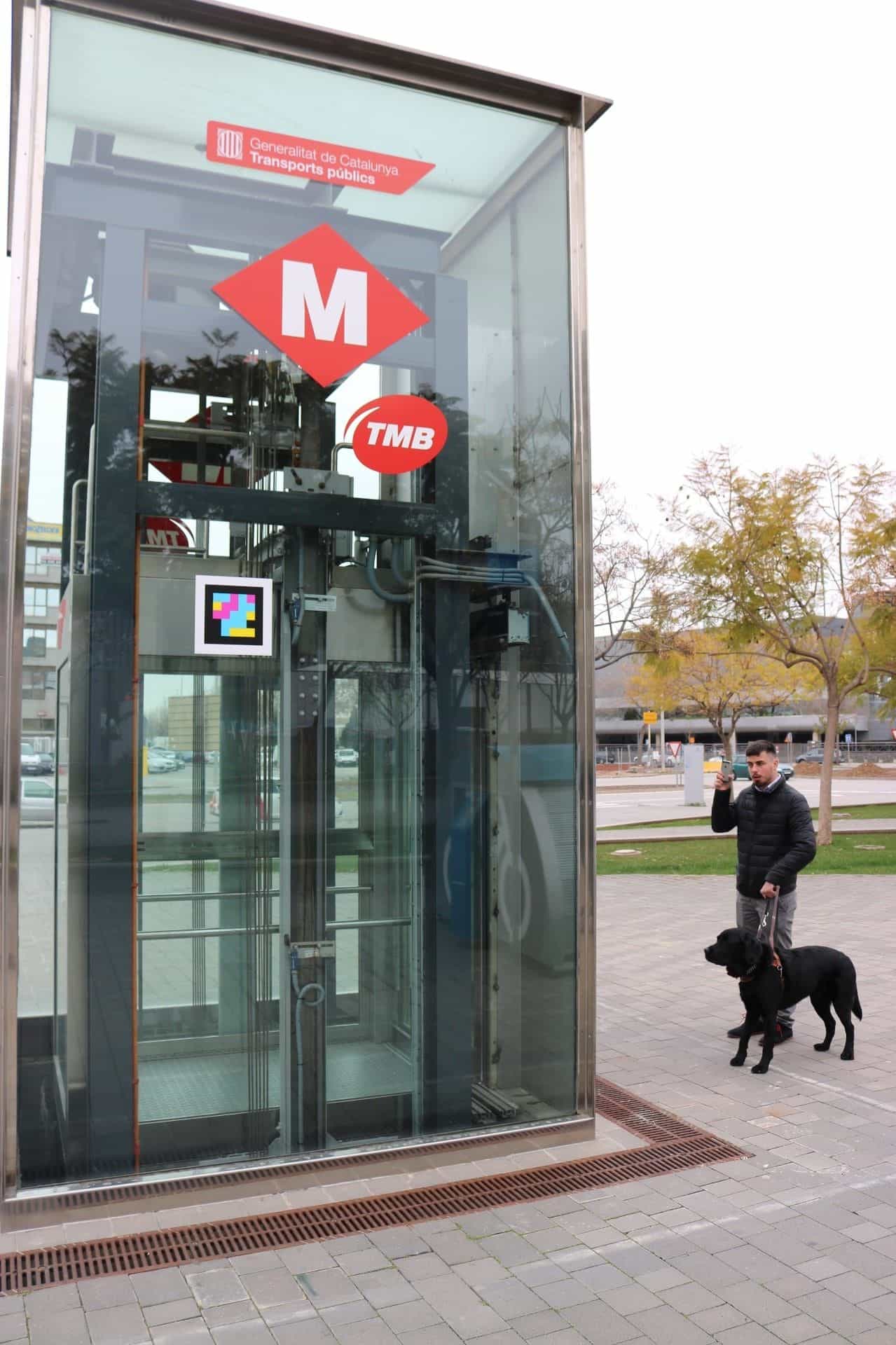 盲導犬を連れた利用者がフィラ駅のTMB街路エレベーターのNaviLensコードをスキャンしている様子
