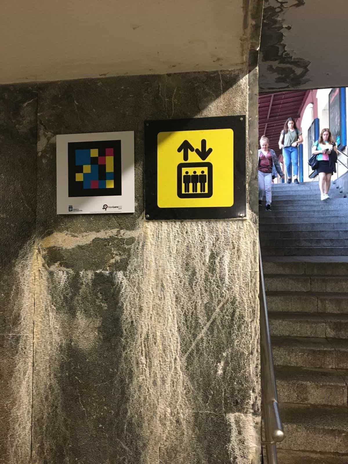 Pictograma amarillo de ascensor sobre columna de mármol con código NaviLens NaviLensGO