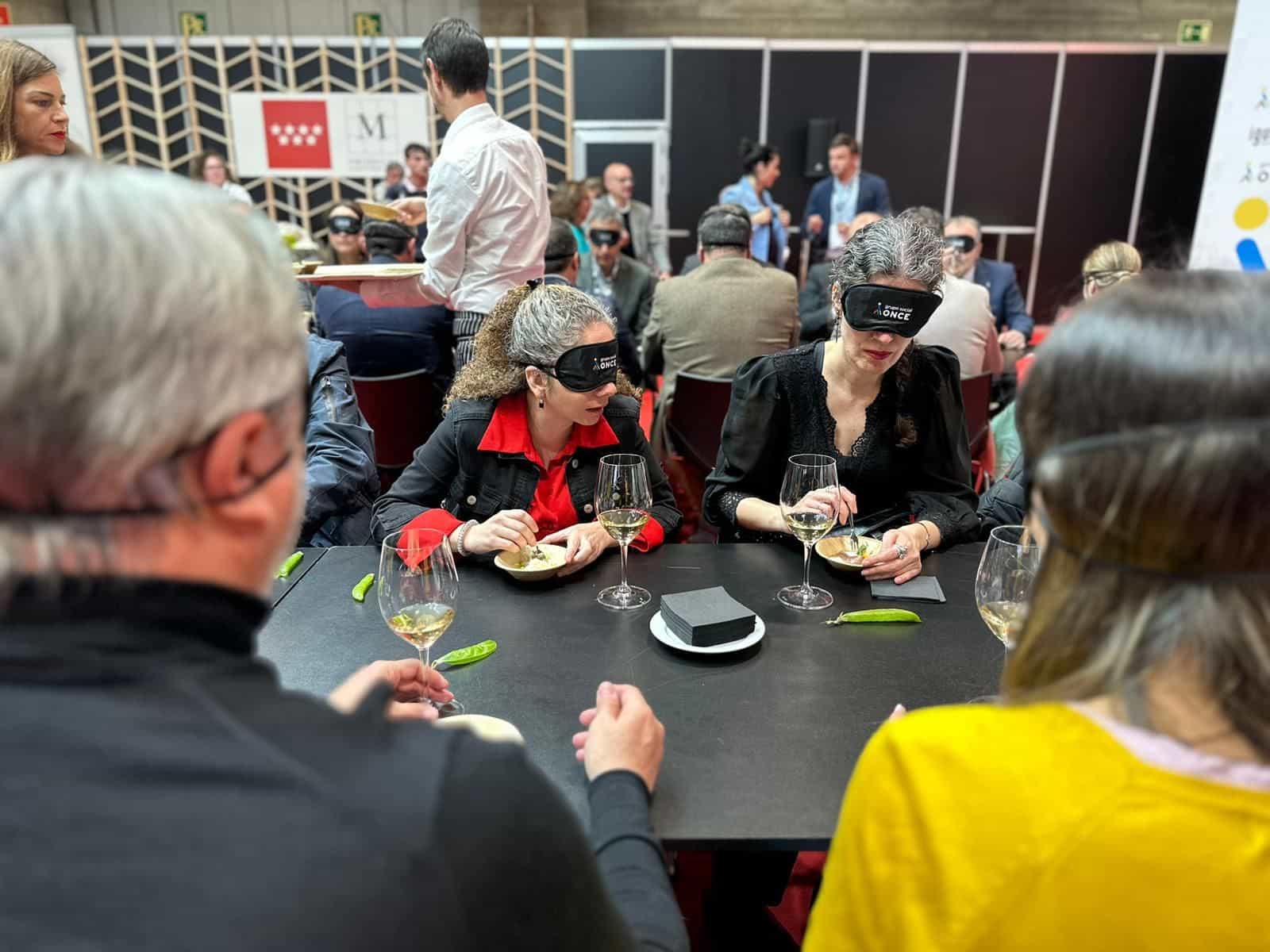 Due partecipanti con mascherine nere del Grupo Social ONCE assaggiano un vino bianco con un piattino di stuzzichini alla degustazione «Activa tus Sentidos» di Decanta Madrid al Salón Gourmets