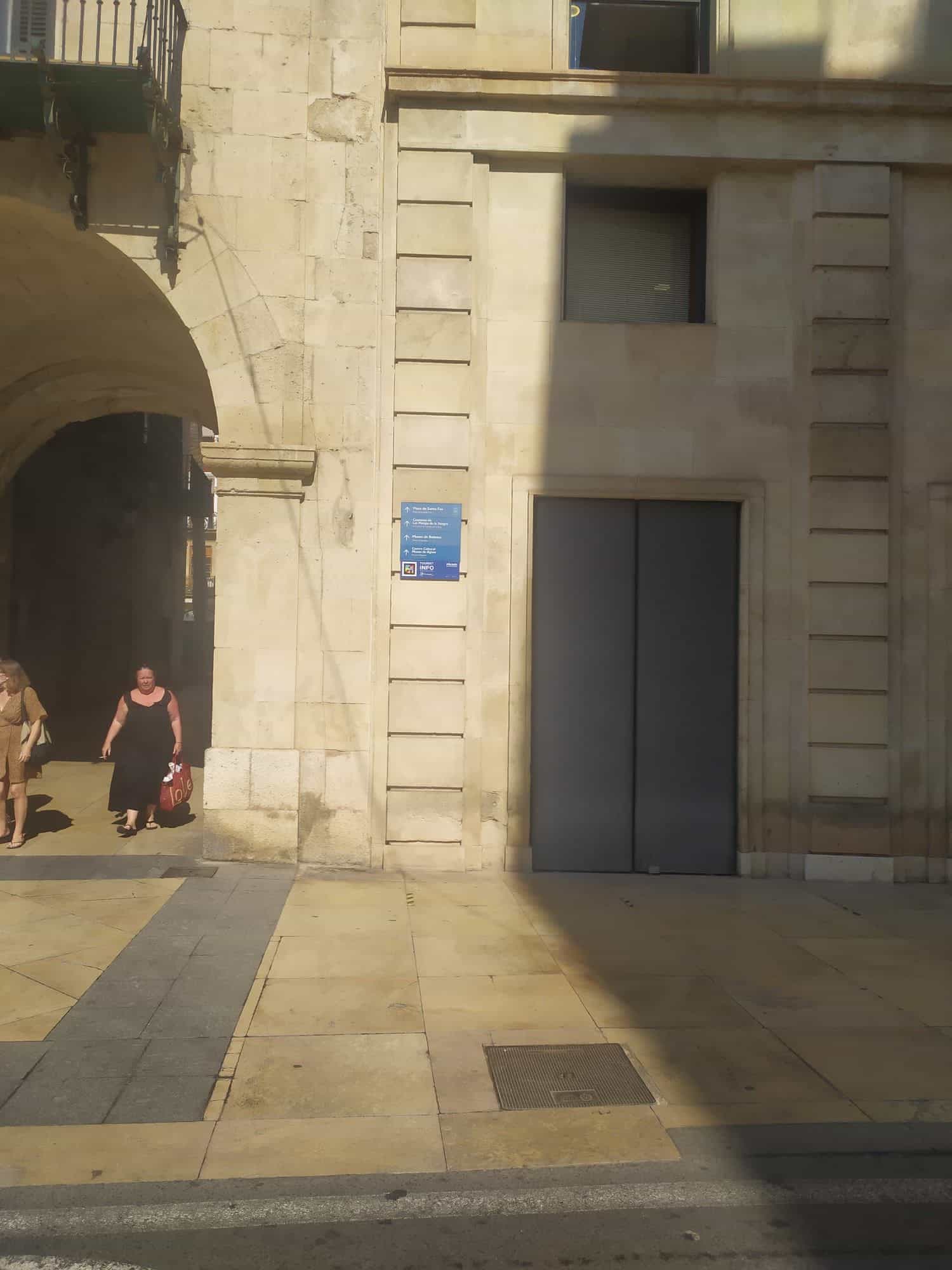 Pfeiler des Rathauses von Alicante mit blauer Tourist-Info-Stele, die auf Plaza de Santa Faz, Kloster Monjas de la Sangre und das Krippenmuseum hinweist