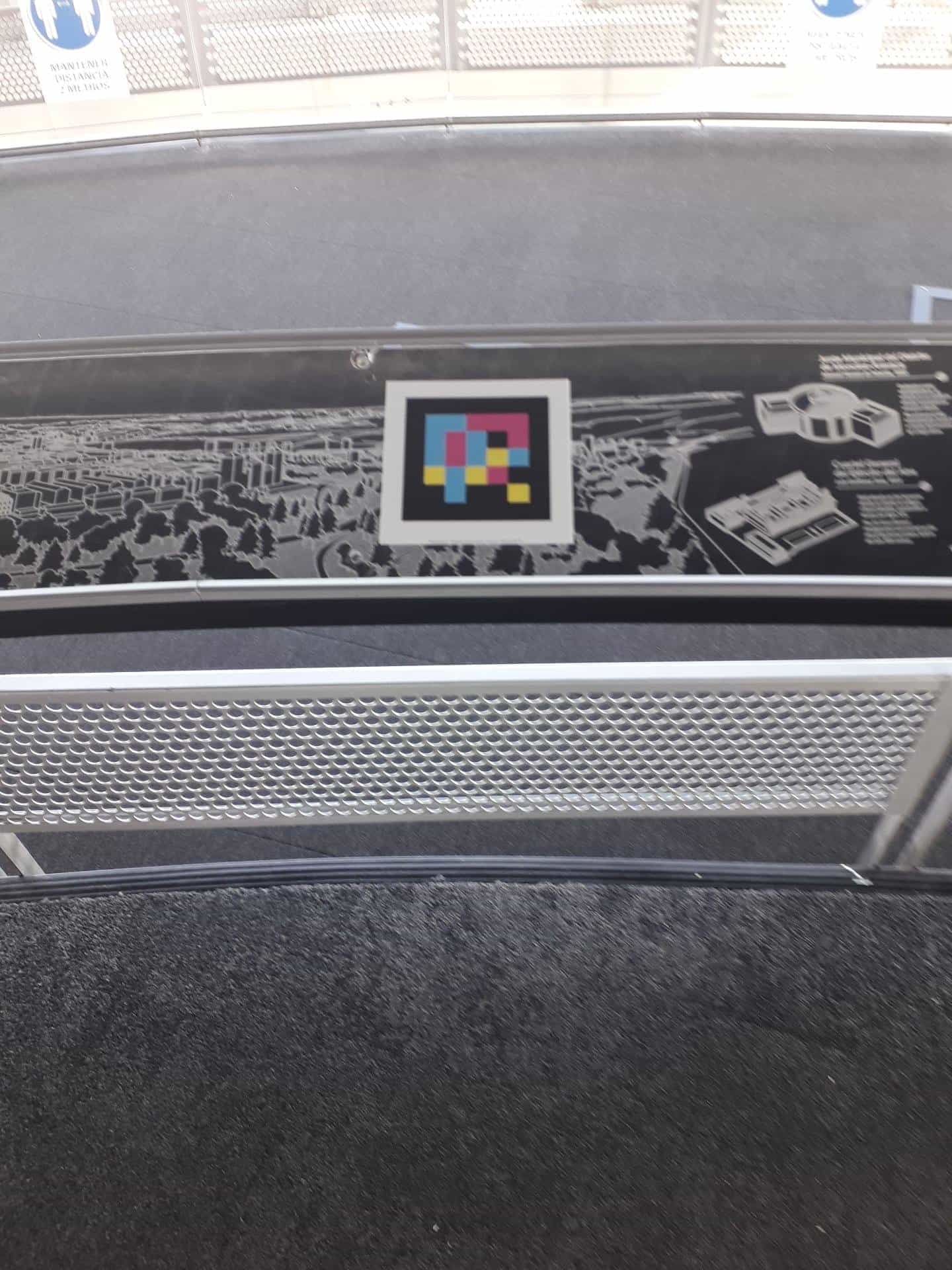 Close-up of a panel on the Faro de Moncloa information railing with an aerial map embossed on a black background; in the centre, a square colour NaviLens code framed in white lets visitors hear the description of the panorama