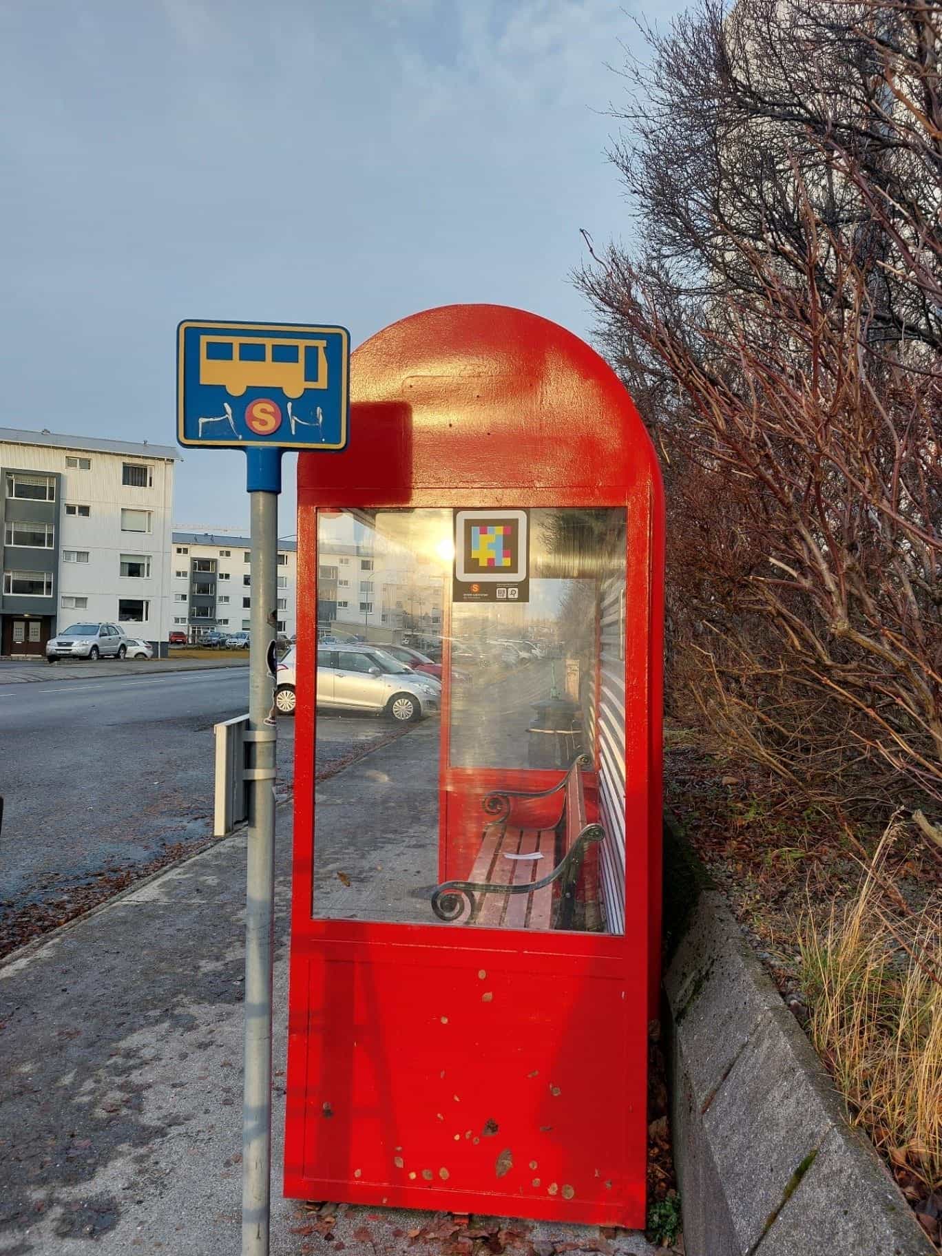 Cabina verticale rossa di Strætó con codice NaviLens applicato sul vetro e cartello islandese di fermata del bus accanto
