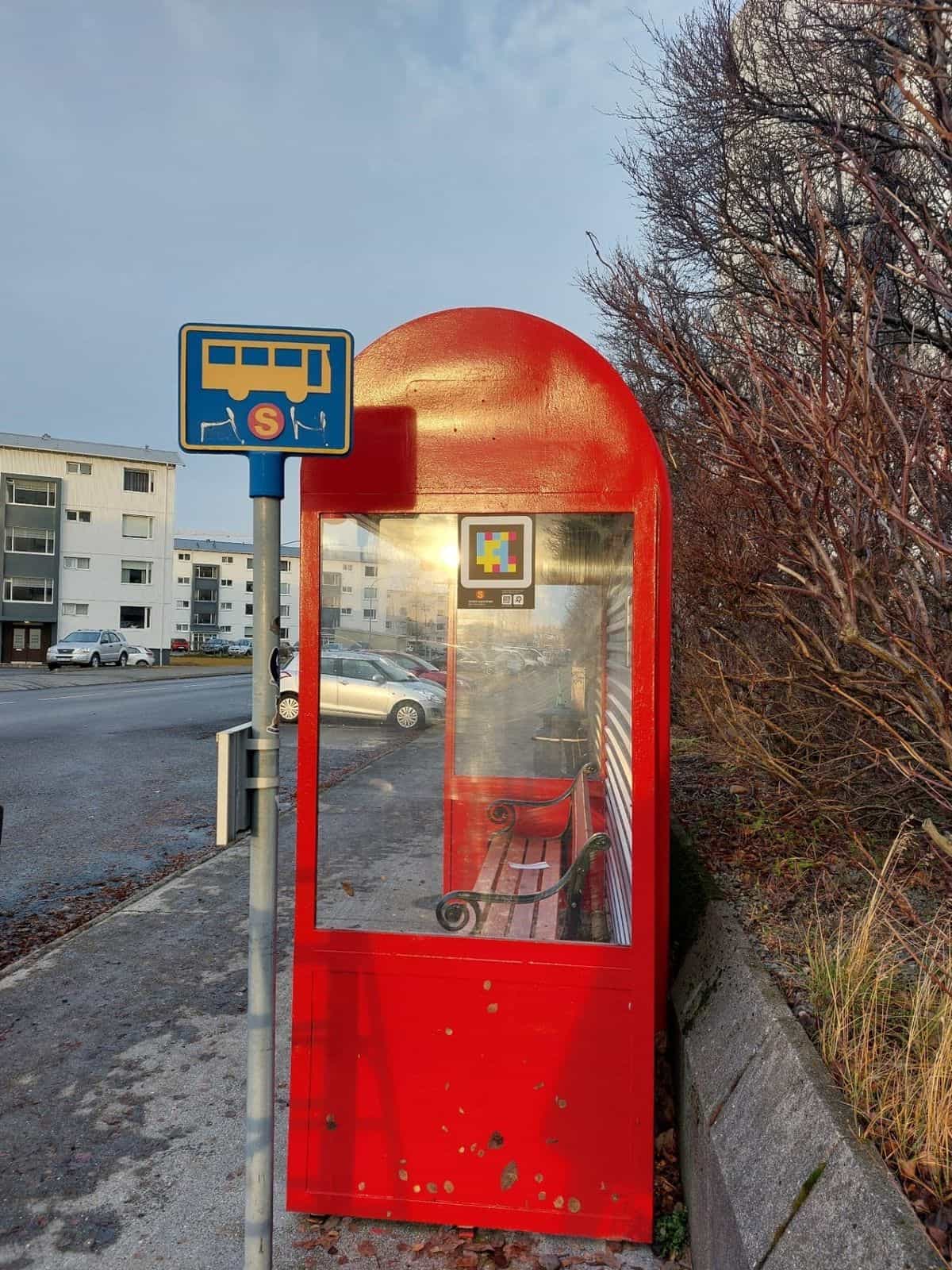 Cabina vertical roja de Strætó con código NaviLens pegado en el cristal y señal islandesa de parada de bus al lado