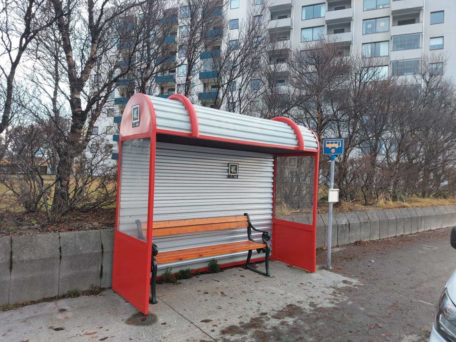 Strætó's signature red bus shelter in Reykjavík with a NaviLens code on the central panel and another on the curved roof headboard