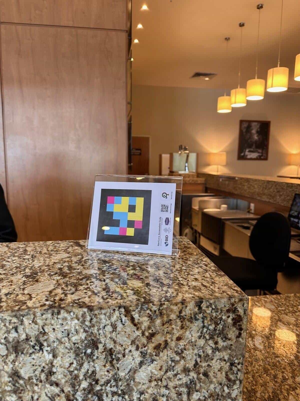 NaviLens sign on the granite counter of the business centre at the Hampton by Hilton Guadalajara Expo, with pendant lights in the background