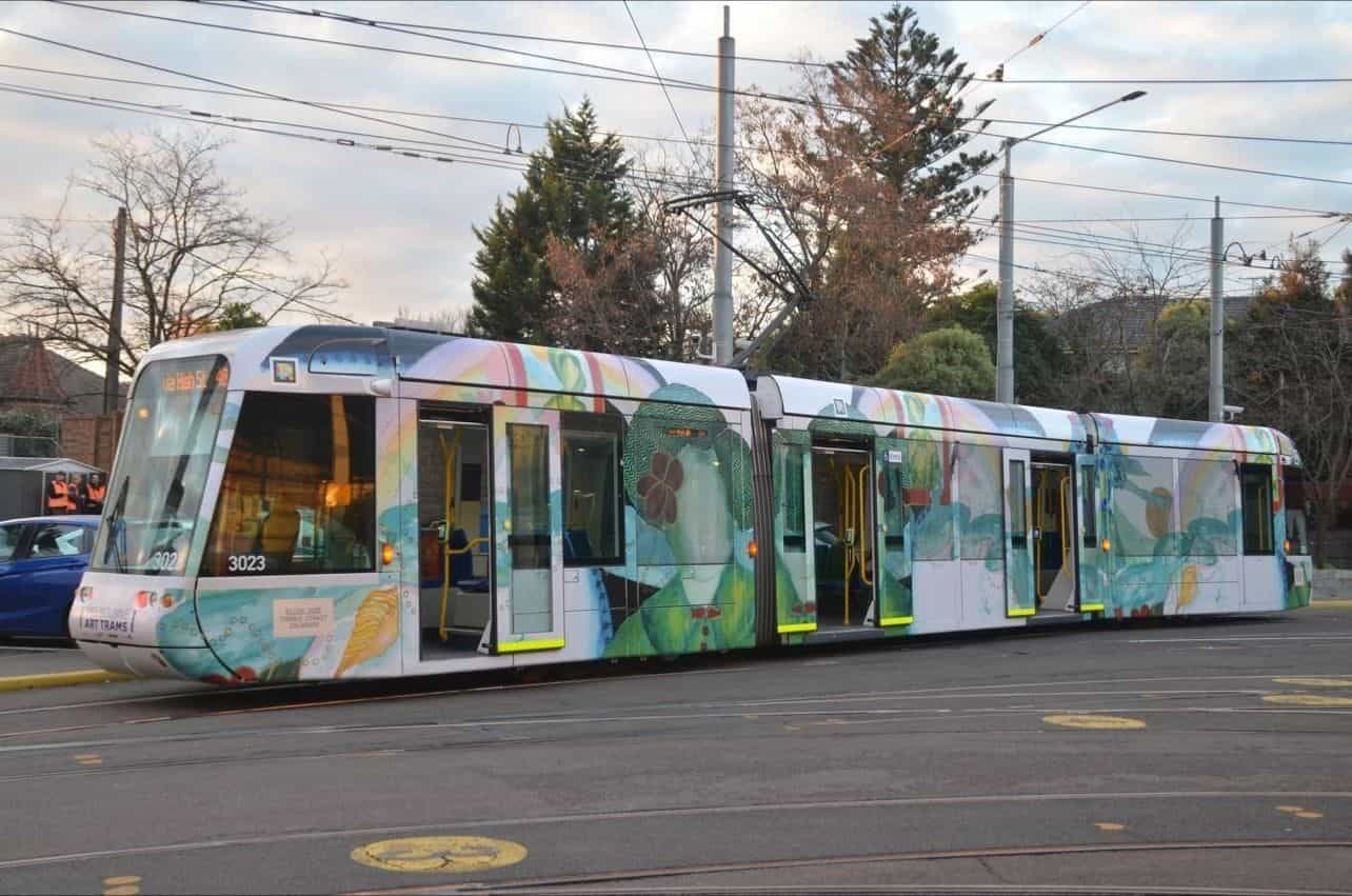 Ellen José のラッピングを纏った C-Class「Art Tram」3023 がメルボルン郊外のロータリーで営業運転中。架線、葉の落ちた木、行先表示「Via Hash St — 48」。運転台脇に白枠の NaviLens コード