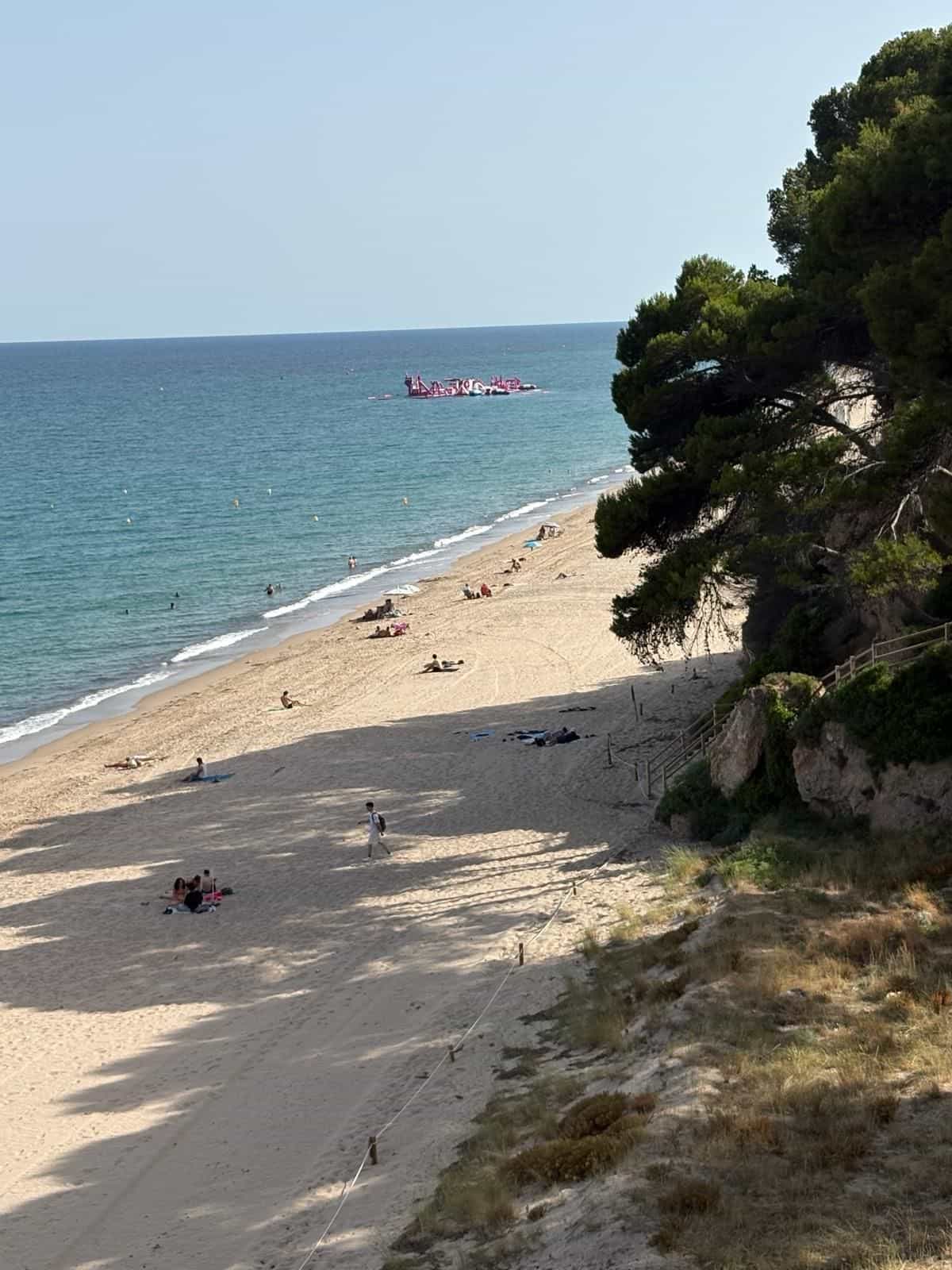 Sandfläche am Passeig de les Cales mit einem vor der Küste verankerten Wasserpark aus Aufblasbaren und einem abgeseilten Pfad durch die Dünen
