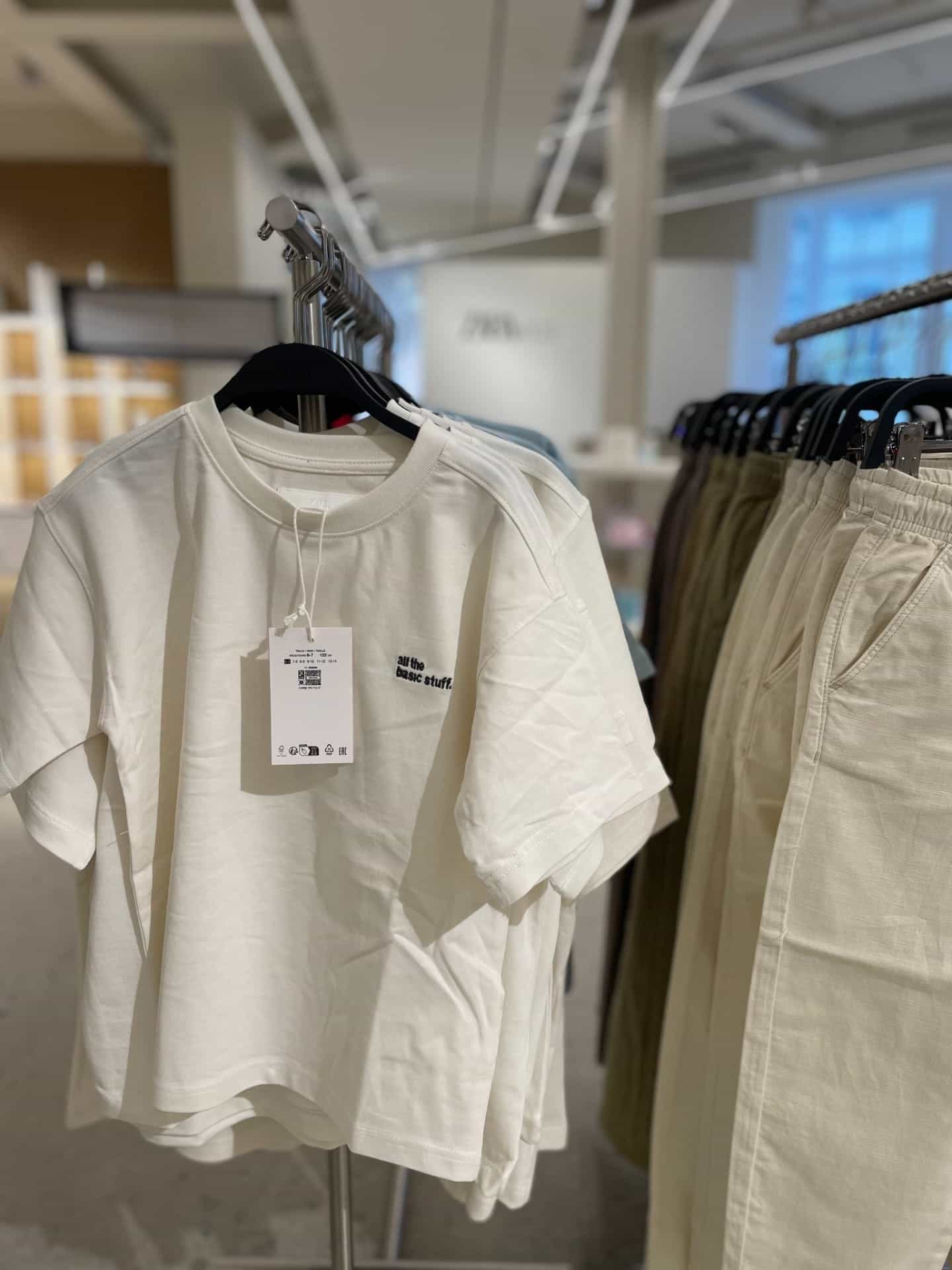Weißes T-Shirt in einem Laden mit sichtbarem bedrucktem Hangtag, in einer realen Verkaufsumgebung.