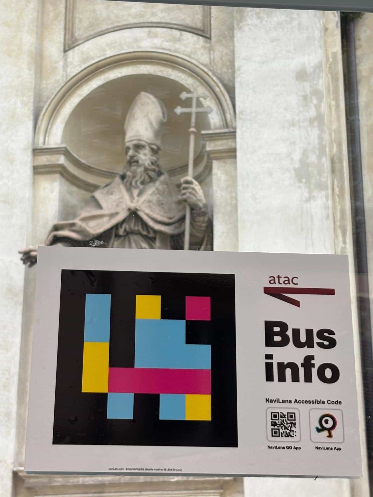 Detail of the ATAC Bus info sign with accessible NaviLens code and download icons for NaviLens GO and NaviLens App on the glass of a central Rome shelter