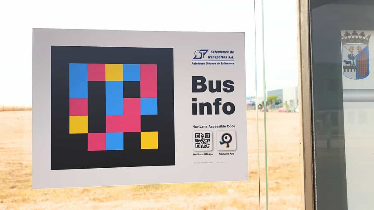 Detalle del cartel Bus info pegado al cristal de una marquesina de Salamanca: código NaviLens grande, logo de Salamanca de Transportes y QR para descargar las apps NaviLens GO y NaviLens