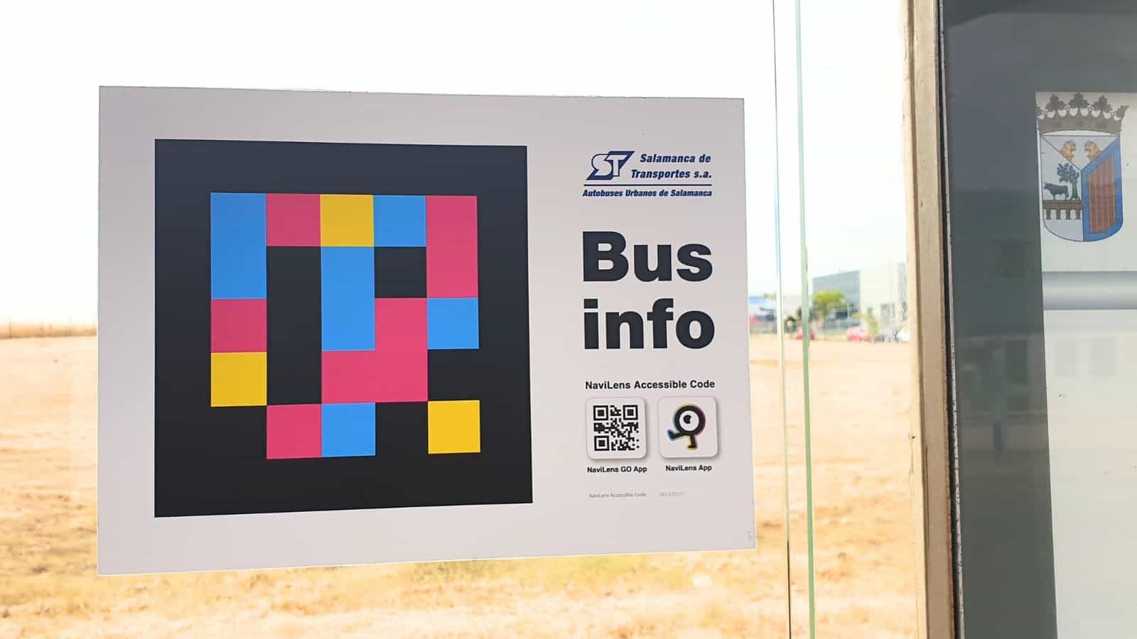 Dettaglio del cartello Bus info applicato al vetro di una pensilina di Salamanca: codice NaviLens grande, logo di Salamanca de Transportes e QR per scaricare le app NaviLens GO e NaviLens