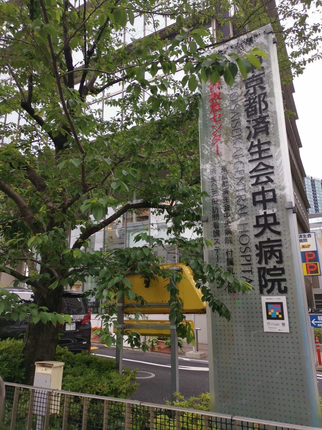 Vertical sign of Tokyo Saiseikai Central Hospital among the cherry trees on the grounds, with a NaviLens code at the bottom