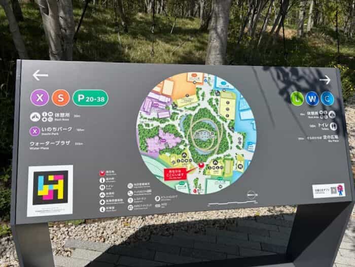 会場の円形マップサインに「いのちパーク / Inochi Park」「ウォータープラザ / Water Plaza」「空の広場 / Sora Plaza」を示すX・S・P・L・W・Cゾーンと、左下に設置されたNaviLensコード