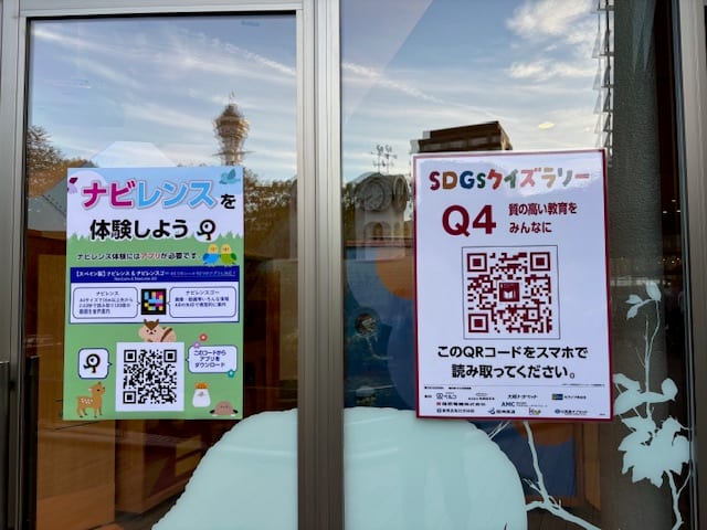 Two posters on the Tennoji Zoo Museum glass door: «ナビレンスを体験しよう» and «SDGsクイズラリー Q4 質の高い教育をみんなに»