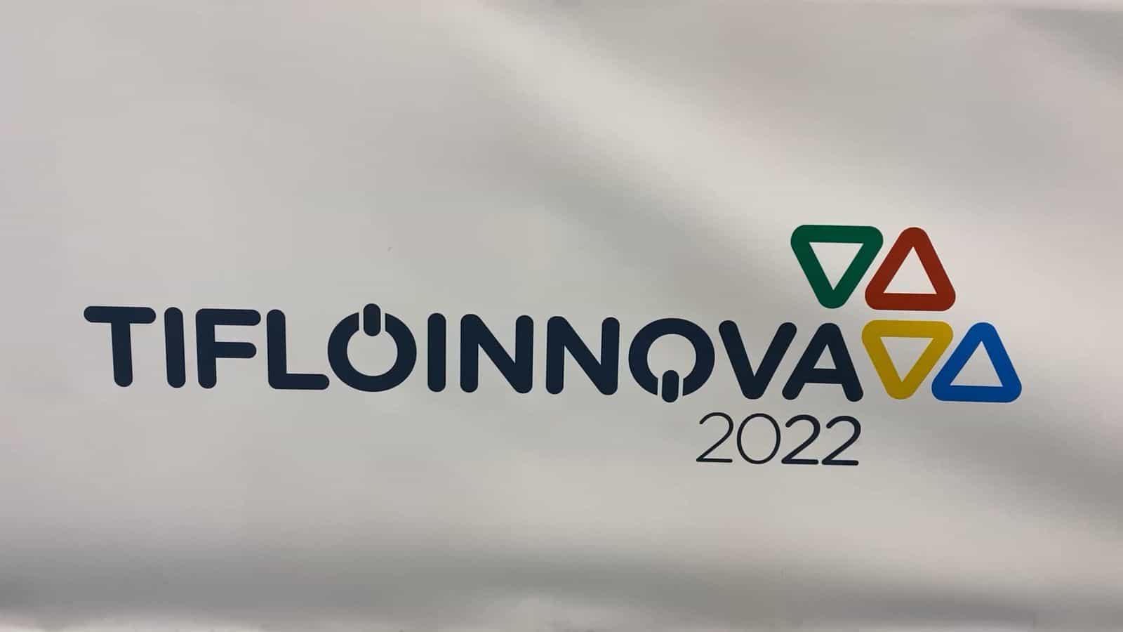 Telone bianco di benvenuto con il logo «TIFLOINNOVA 2022» in blu scuro, il simbolo di power dentro la lettera O e il marchio formato da quattro triangoli verde, rosso, giallo e azzurro a destra del nome
