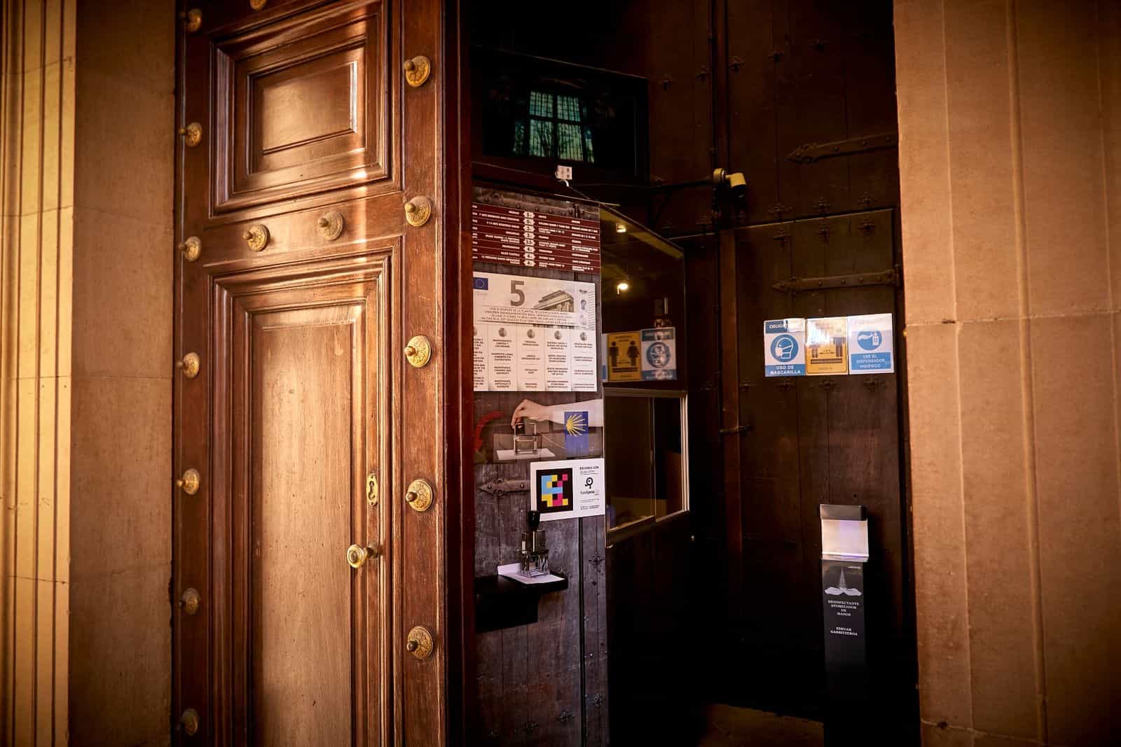 Puerta de acceso a la Catedral de Pamplona con código NaviLens junto al panel de tarifas, accesibilidad para peregrinos del Camino de Santiago