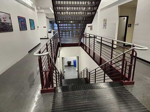 Central staircase of an academic building at NIU with red railings, overhead view of the landing and framed signs in the hallways