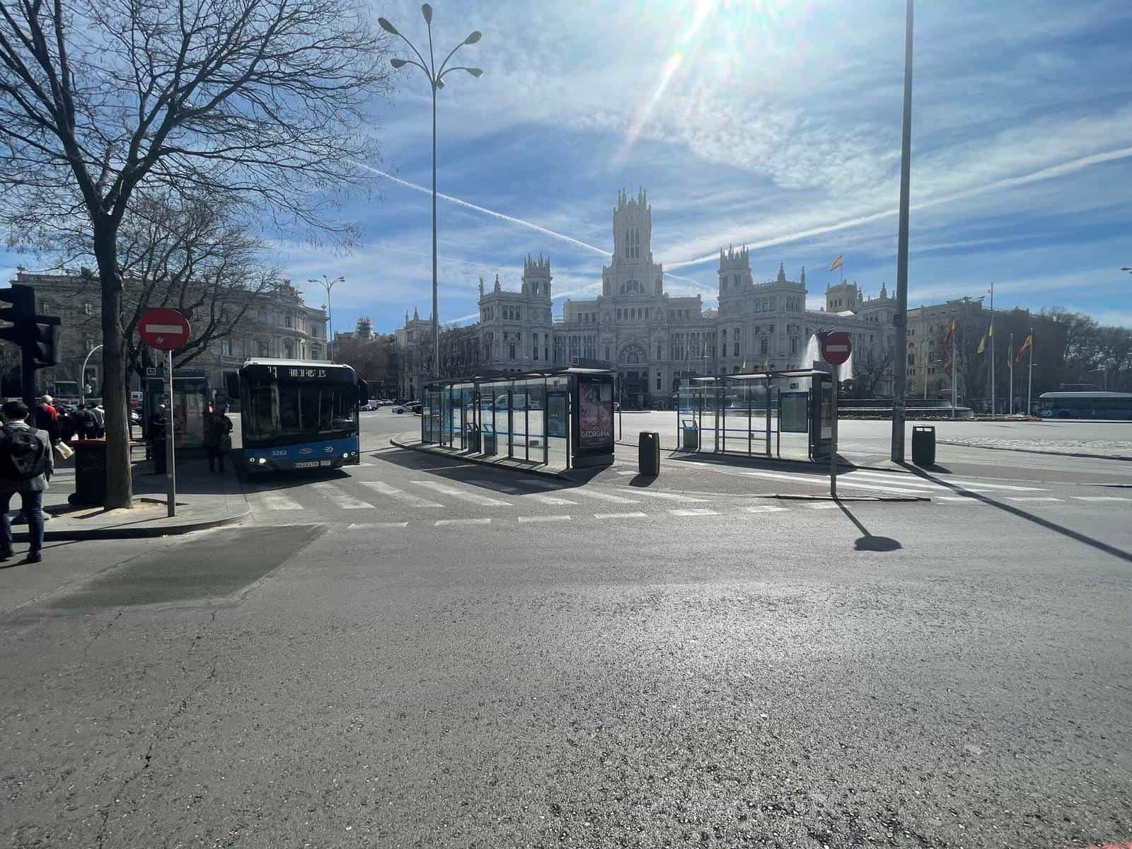 Plaza de Cibeles with several EMT shelters lined up on the median, a blue bus no. 3262 parked and, in the background, the Palacio de Comunicaciones under a clear sky: one of Madrid's busiest stops, part of the NaviLens network