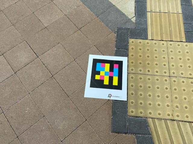 NaviLens GO tag on the brick paving at a crossing of yellow tactile lines (guidance + warning) on the pedestrian route between the Port Liner and the Bandō Kobe Science Museum