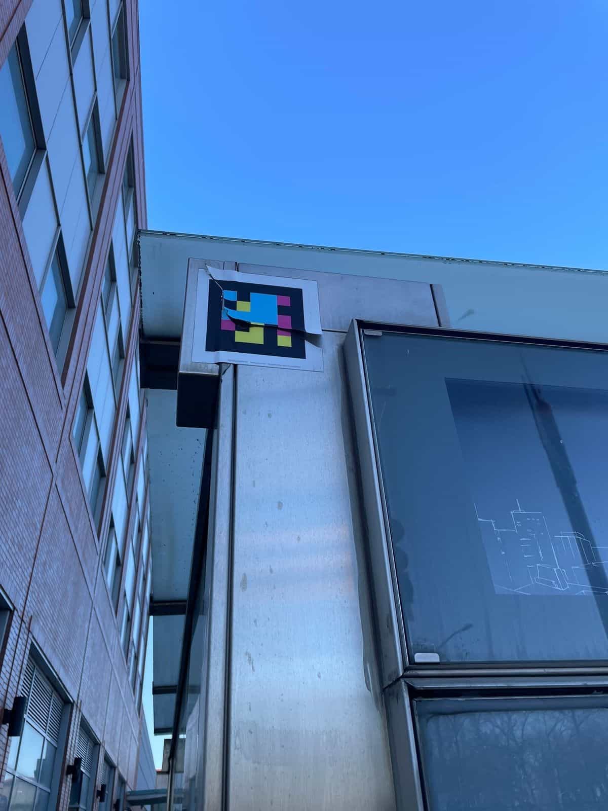Código NaviLens impreso y fijado en la coronación superior de una marquesina metálica del Bronx, captado en contrapicado junto a un edificio residencial