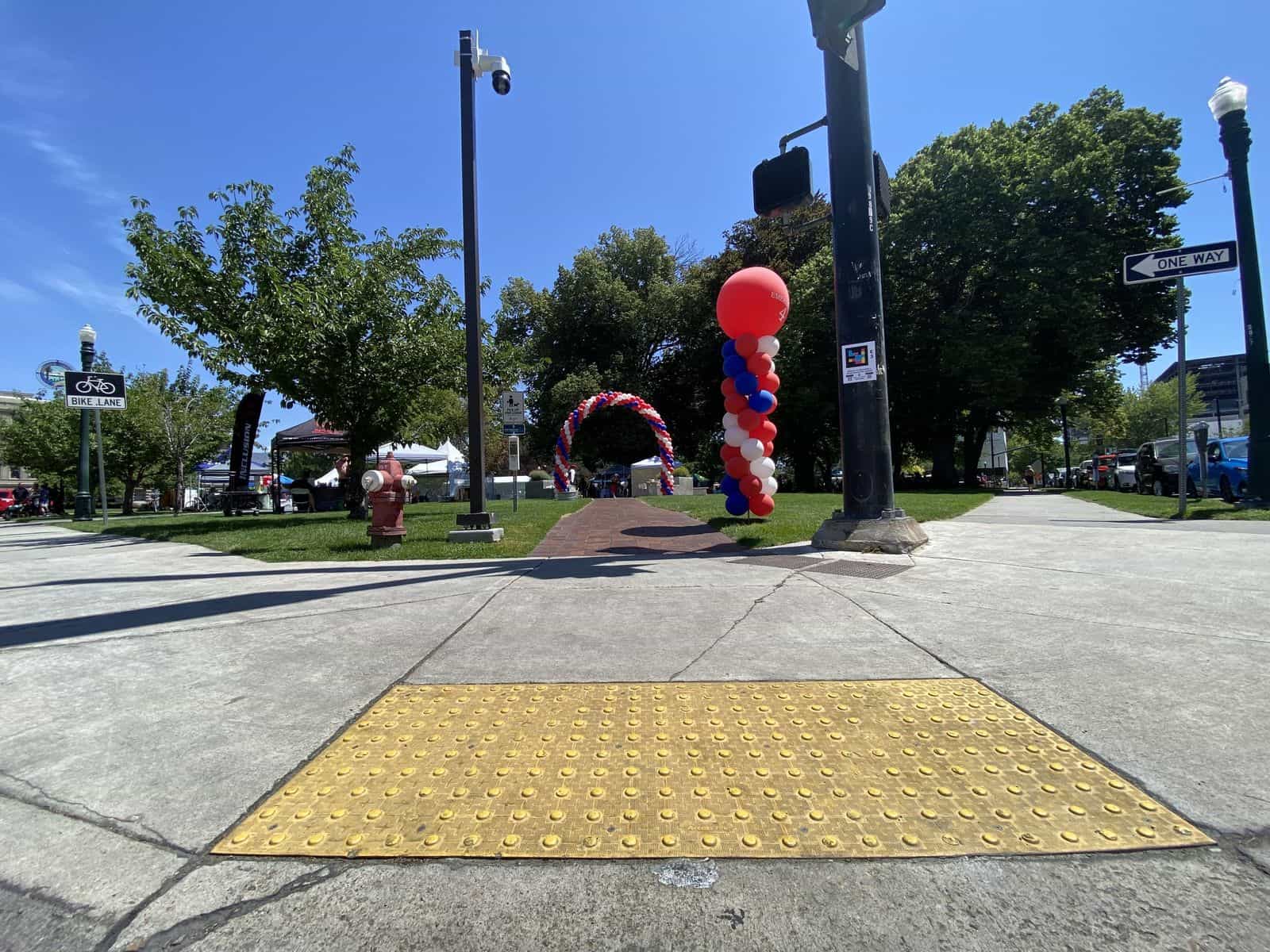 Ampelmast am Kapitol von Idaho mit dem NaviLens-Aufkleber „E3“ und dem Text „Welcome to / Bienvenido a Hands Around the Capitol!“; dahinter ein Bogen aus roten, weißen und blauen Luftballons