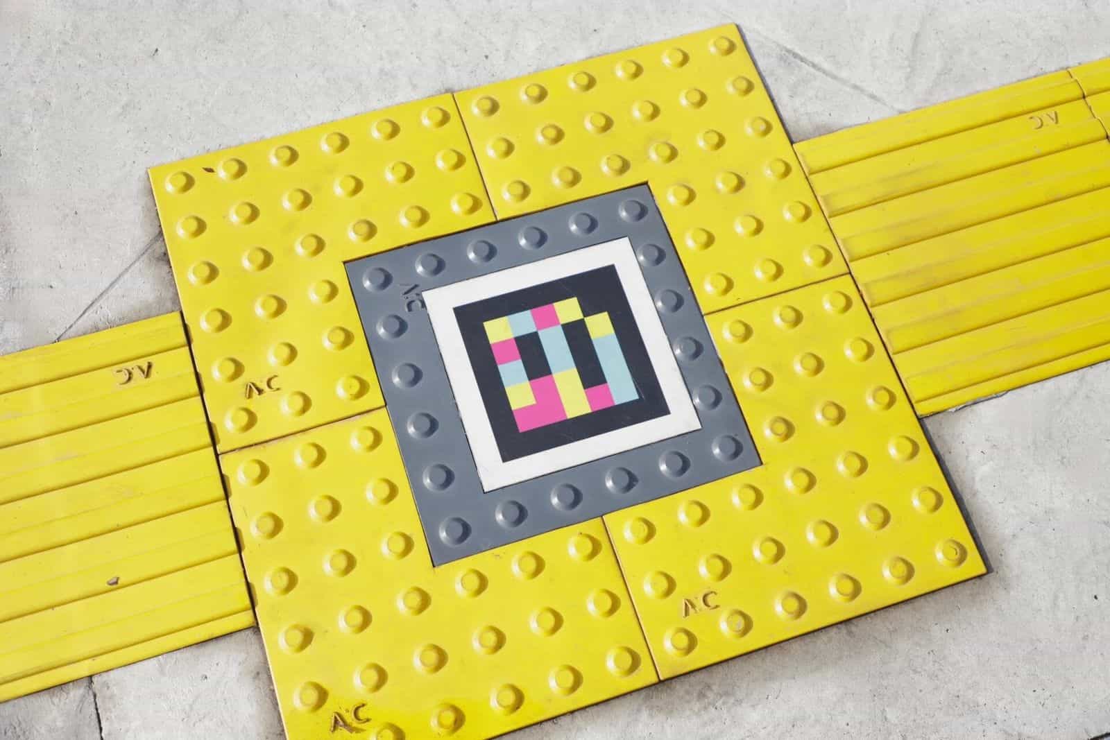 NaviLens code framed at the centre of a yellow cross-shaped tactile paving mosaic on the floor at the entrance to the Zapopan Passport Office
