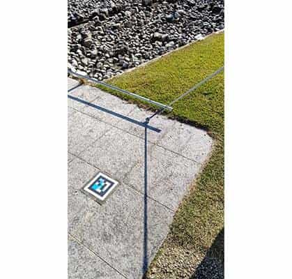 Top-down view of a NaviLens code stuck at the boundary between a granite slab and the lawn and gravel area of the sculpture garden
