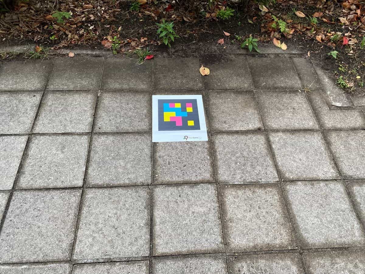 バンドー神戸青少年科学館の庭の地面に設置された大判のNaviLens GOタグ、背景に紅葉と植栽