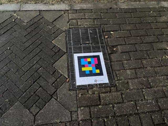 NaviLens GO tag printed on a drainage grate embedded into herringbone paving, showing the code is still readable even on perforated metal surfaces