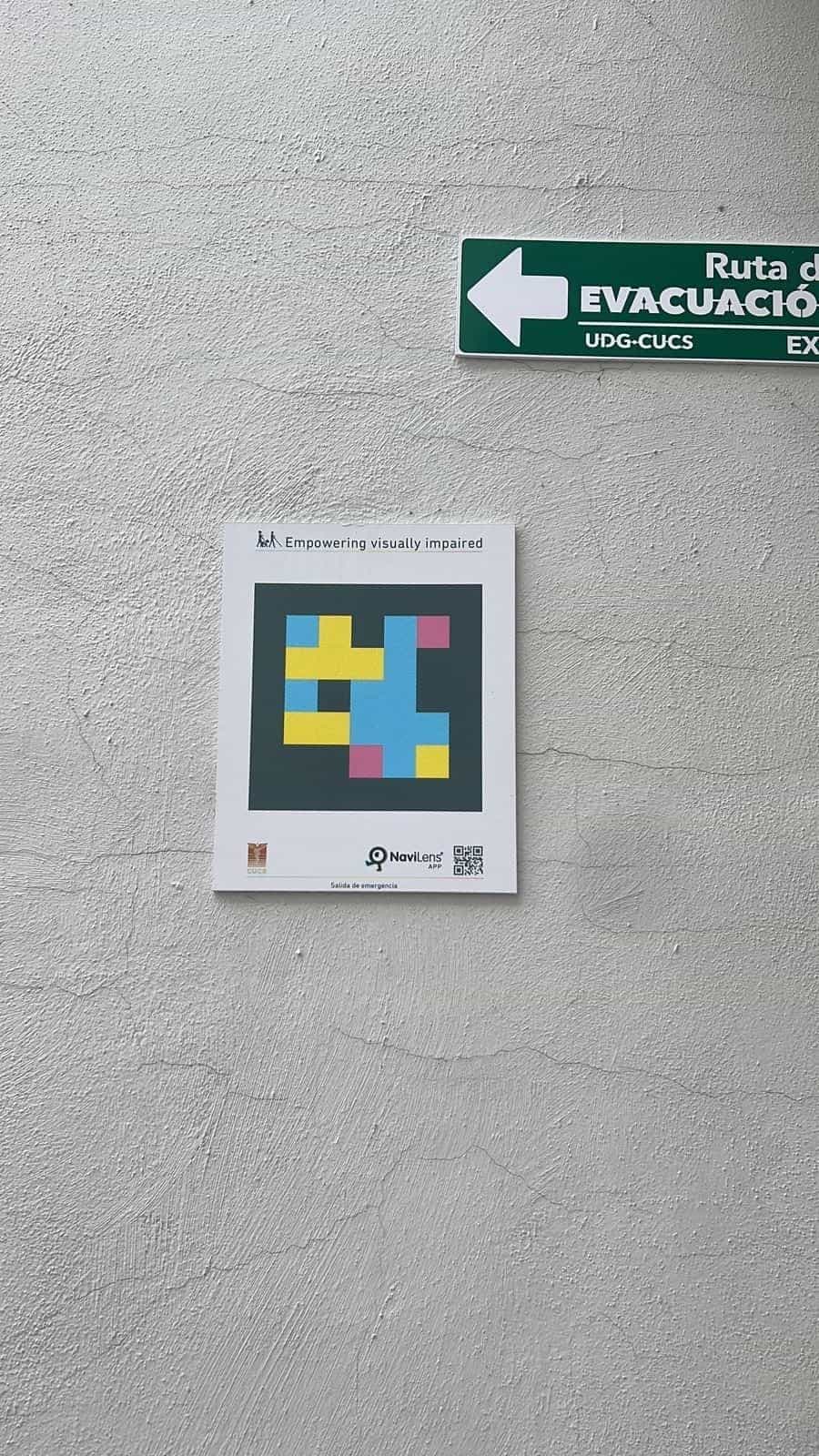 CUCS whitewashed wall with a square NaviLens sign next to a green “UDG-CUCS Evacuation Route” plate.