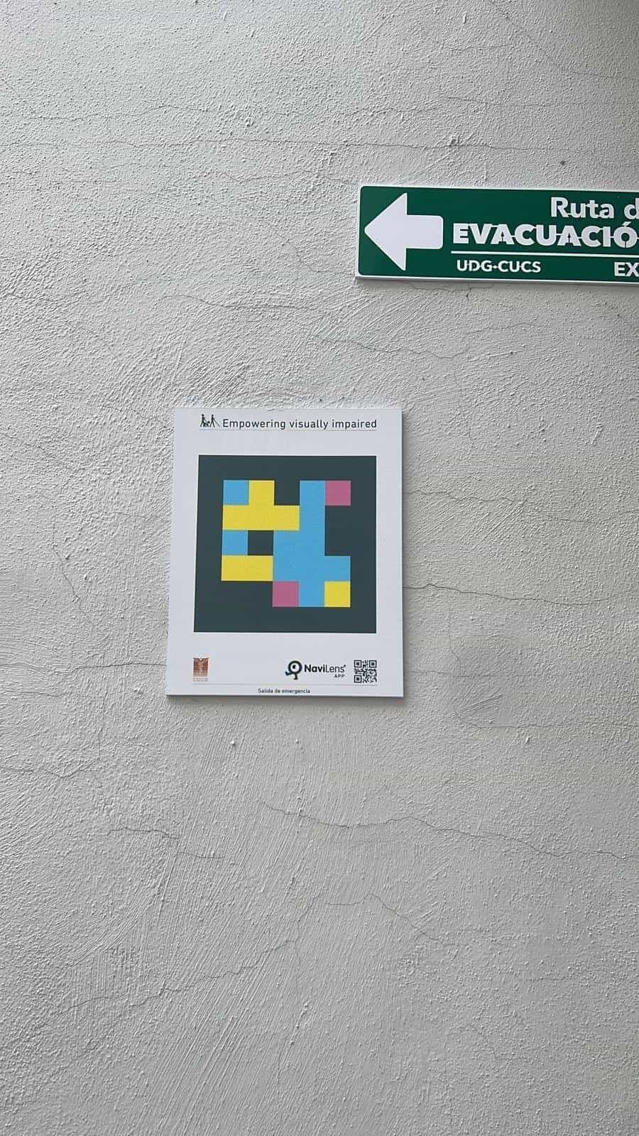 CUCS whitewashed wall with a square NaviLens sign next to a green “UDG-CUCS Evacuation Route” plate.