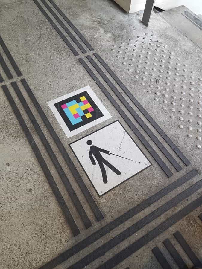 Bodendetail in Versailles-Chantiers: taktile Streifen um einen NaviLens-Code und Piktogramm einer Person mit Stock