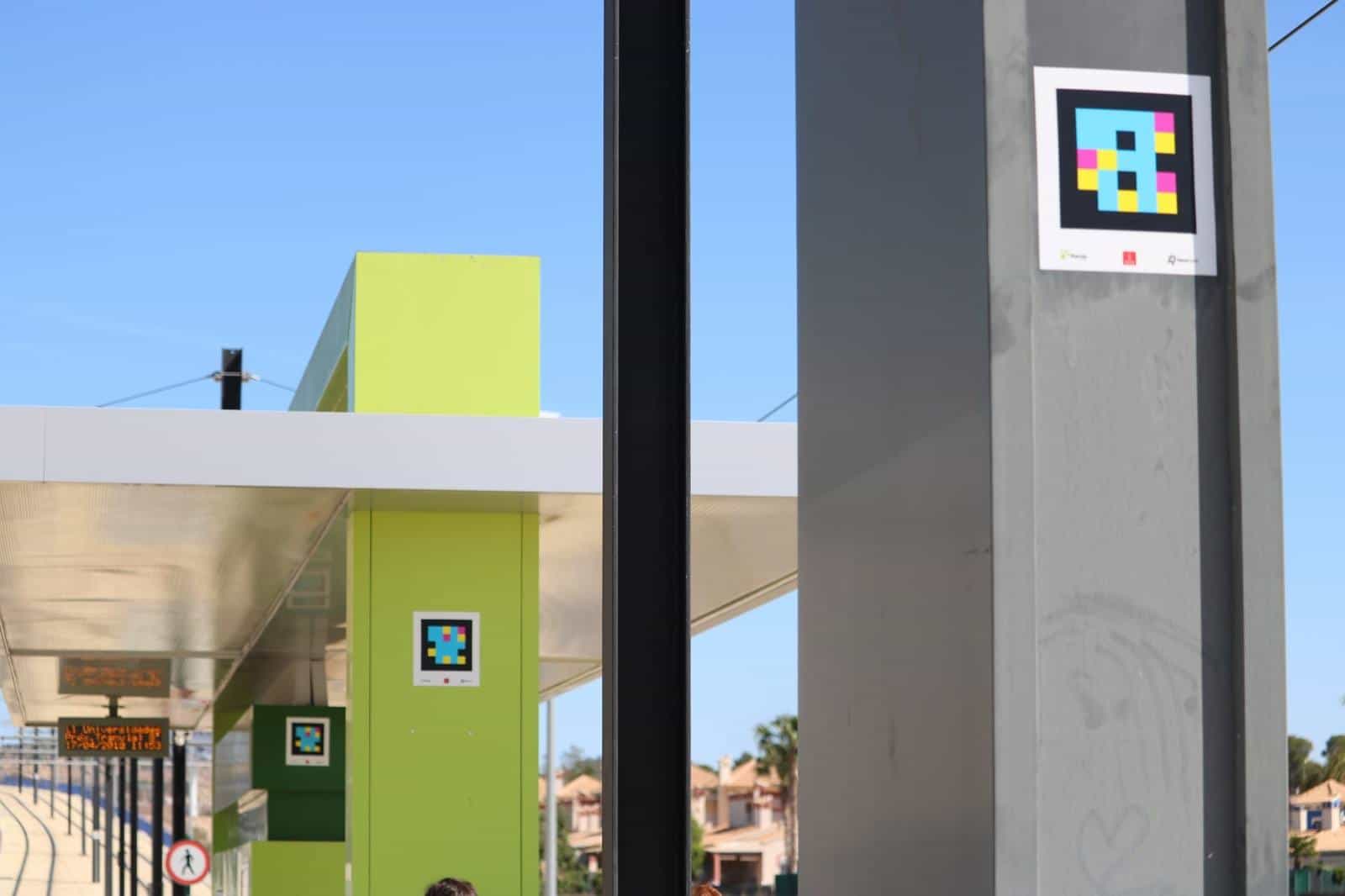 Person scanning a NaviLens code on top of a Murcia Tram shelter, with the LED arrivals screen in the background