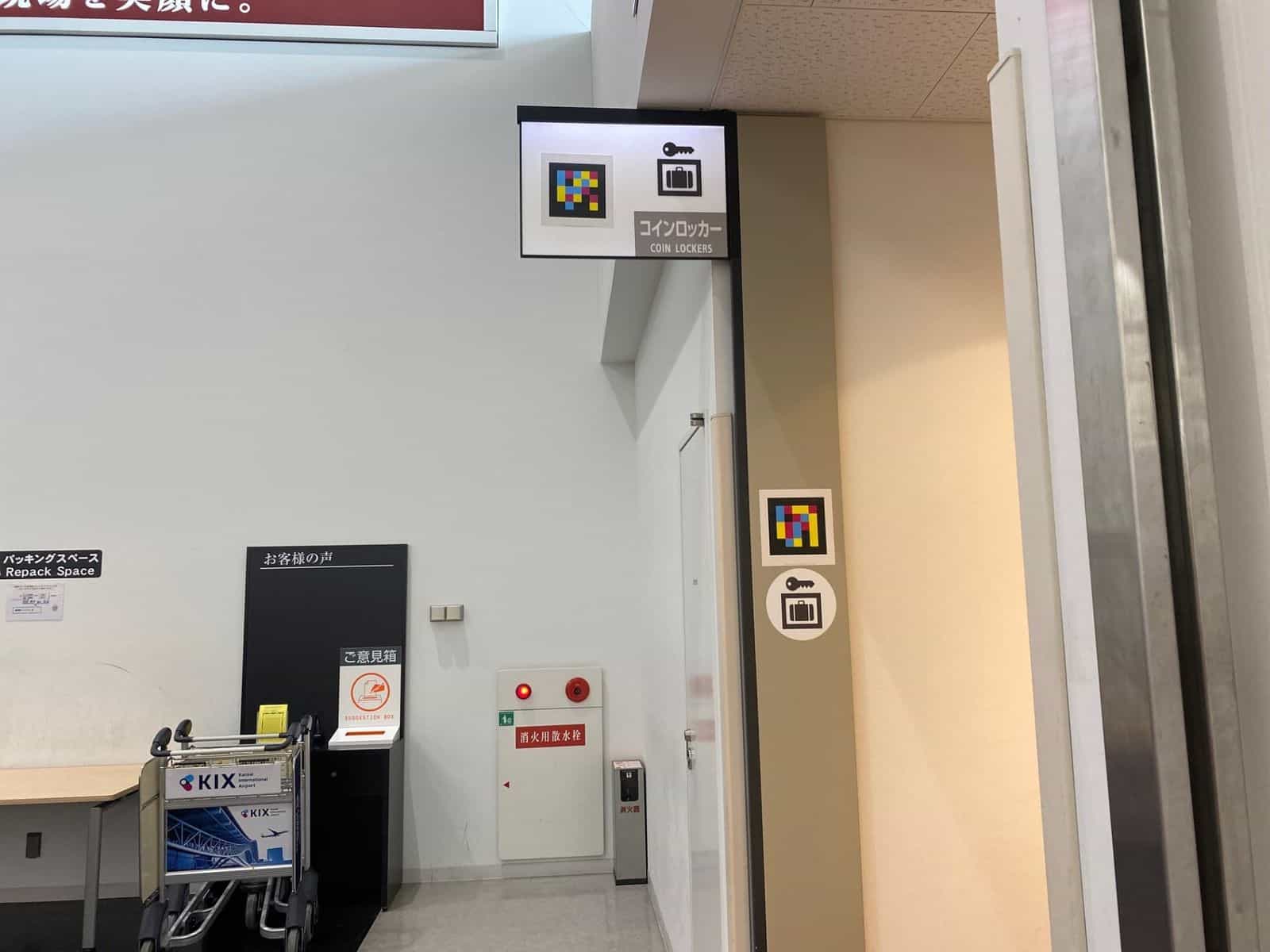 «COIN LOCKERS»-Schild im Kobe Airport mit Schlüssel-Koffer-Piktogramm und NaviLens-Tag, plus zweiter Tag in Stockhöhe