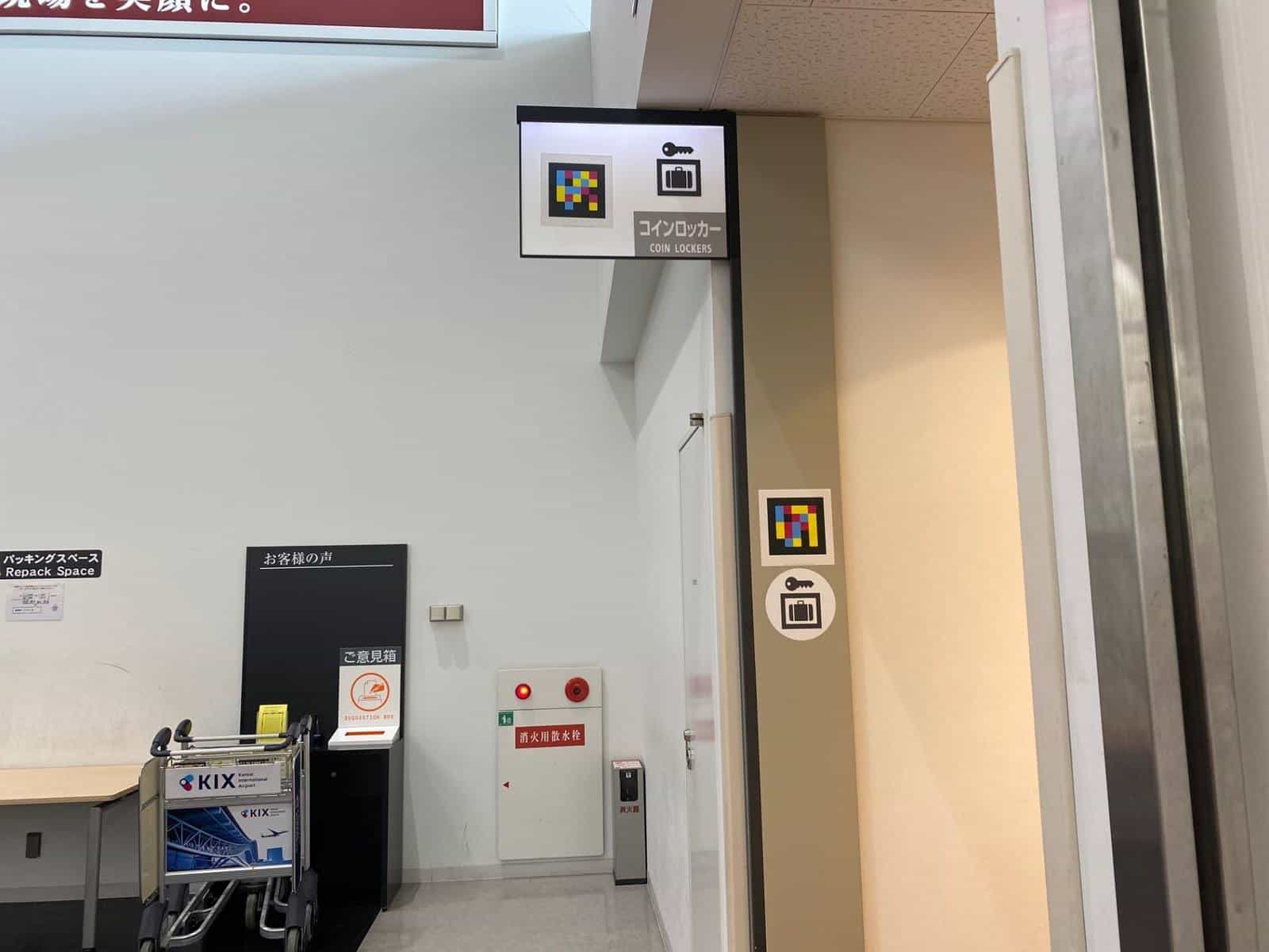 “COIN LOCKERS” sign at Kobe Airport with key-suitcase pictogram and NaviLens tag, plus a second tag at cane height