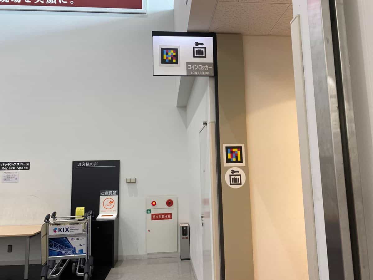 «COIN LOCKERS»-Schild im Kobe Airport mit Schlüssel-Koffer-Piktogramm und NaviLens-Tag, plus zweiter Tag in Stockhöhe