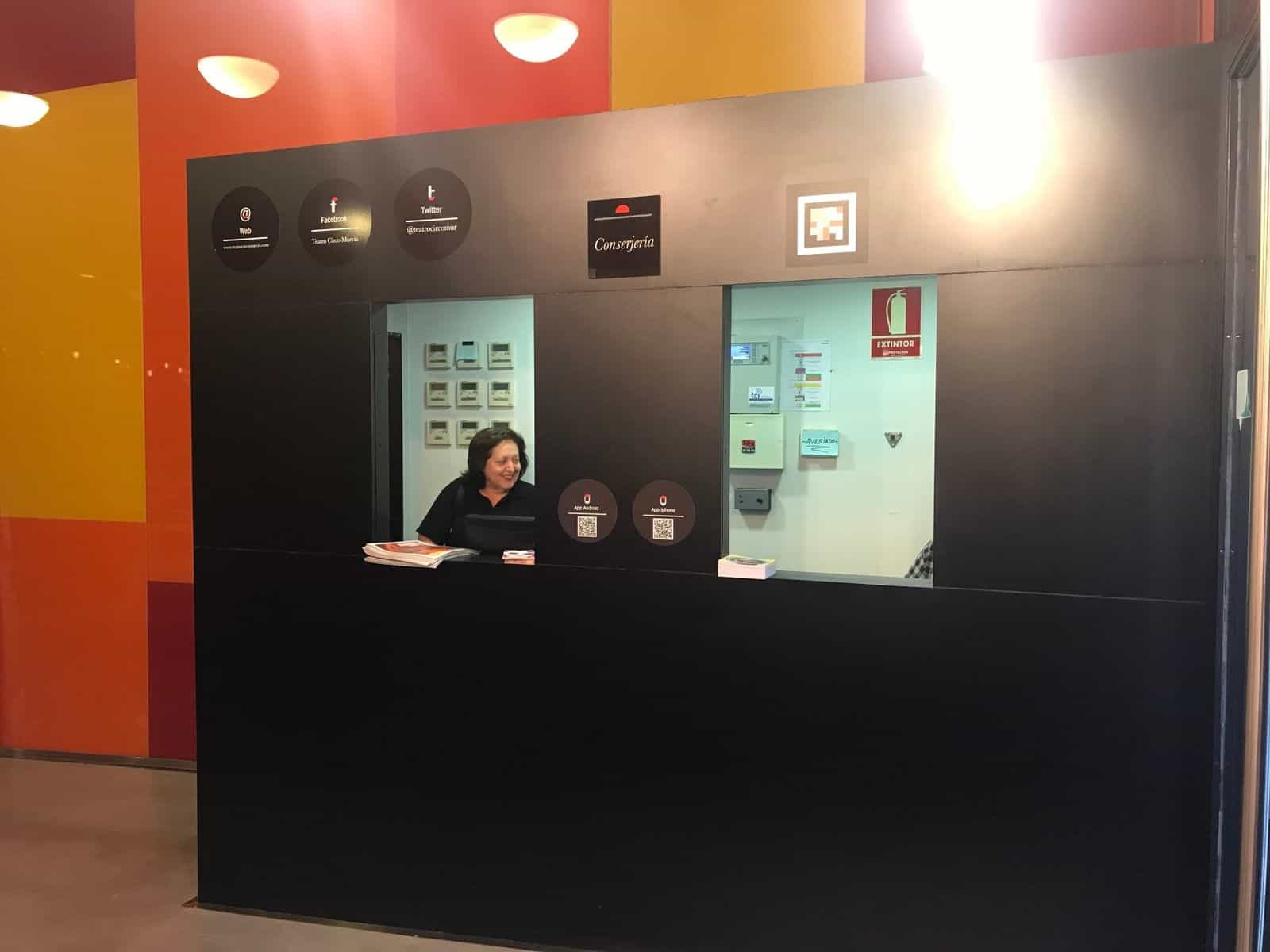 Banco della portineria del Teatro Circo con insegna, icone e un grande codice NaviLens accanto ai QR di download