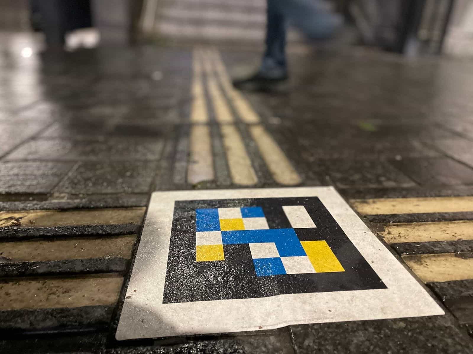 Bodendetail eines NaviLens-Codes in Amsterdam Centraal, integriert zwischen den gelben taktilen Leitlinien