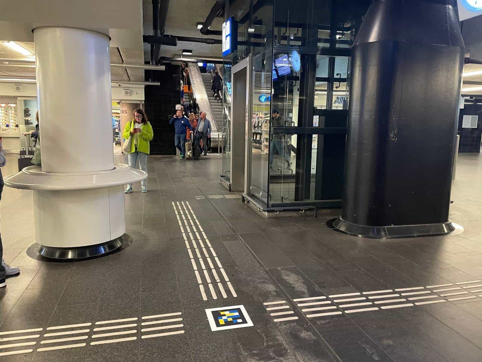 Interior corridor of Amsterdam Centraal with tactile guide lines and a colour NaviLens code embedded in the floor, next to the lift