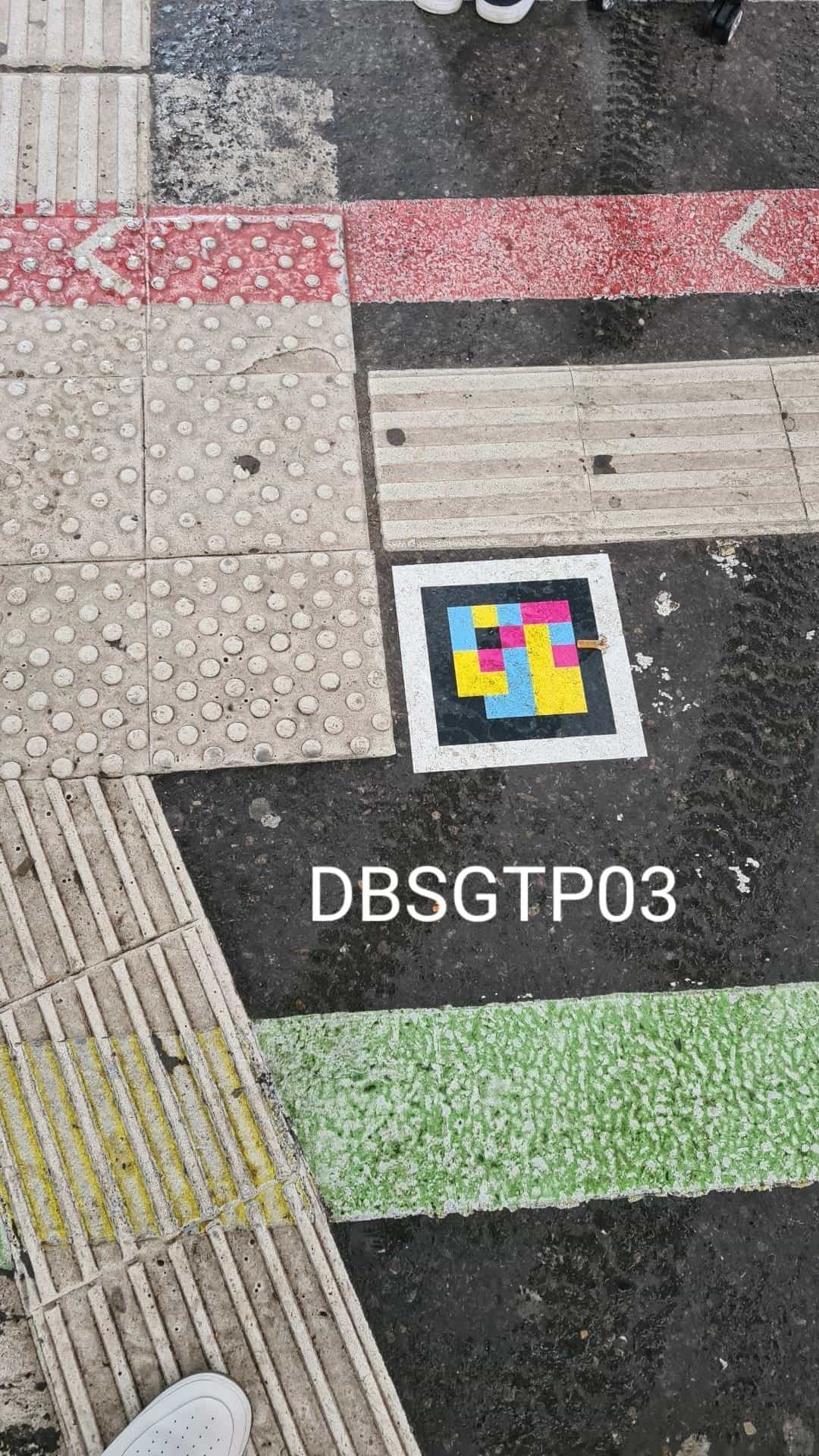 Carrefour près du Hbf avec dalles podotactiles rouges, bande verte de piste cyclable, bande jaune piétonne et code NaviLens au centre (DBSGTP03)