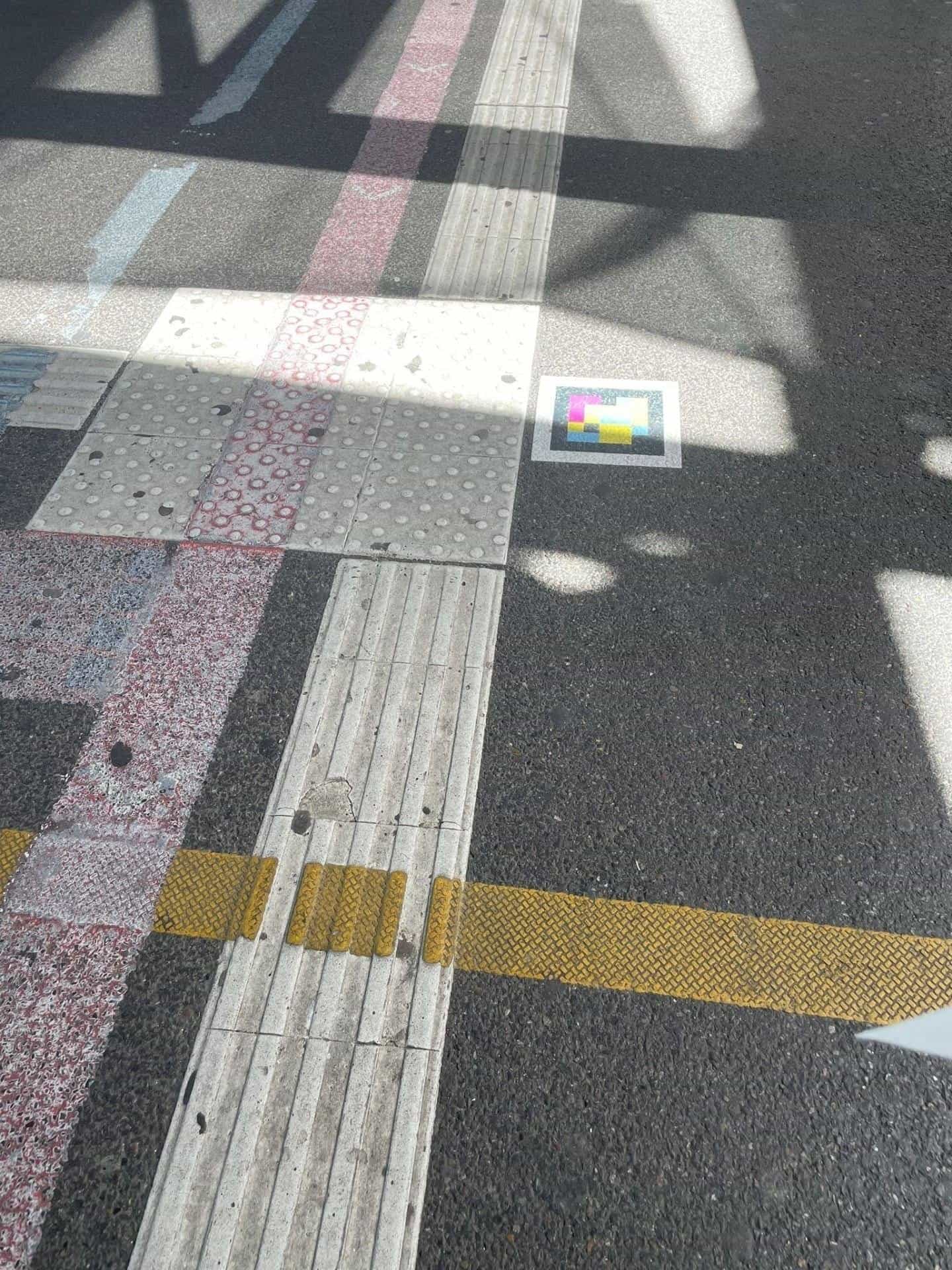Floor of a pedestrian crossing next to Stuttgart Hbf with tactile slabs and a NaviLens code stuck next to the kerb