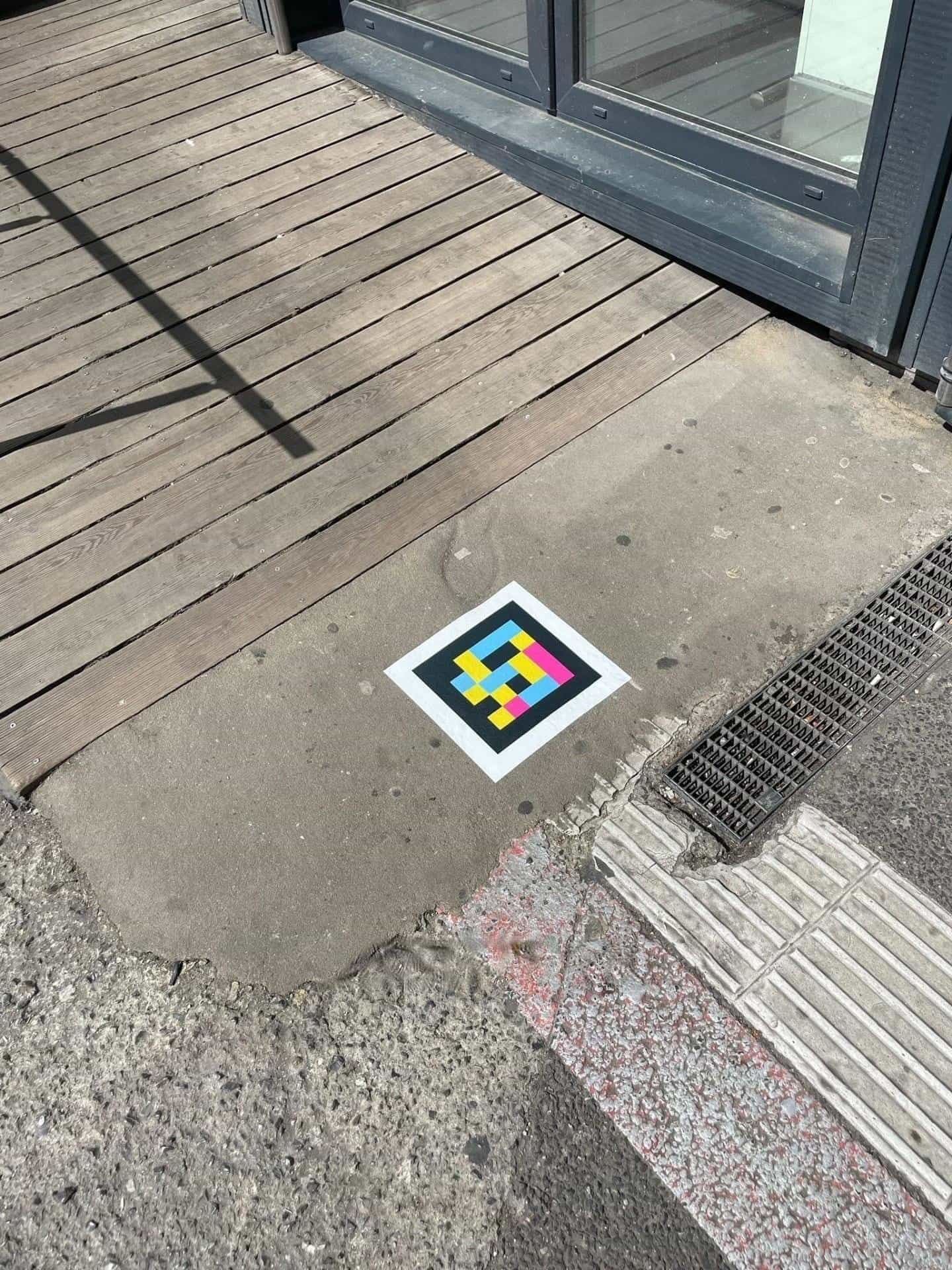 Access to a shop in the Hbf: wooden deck, channelling strip and a NaviLens square code stuck to the polished concrete