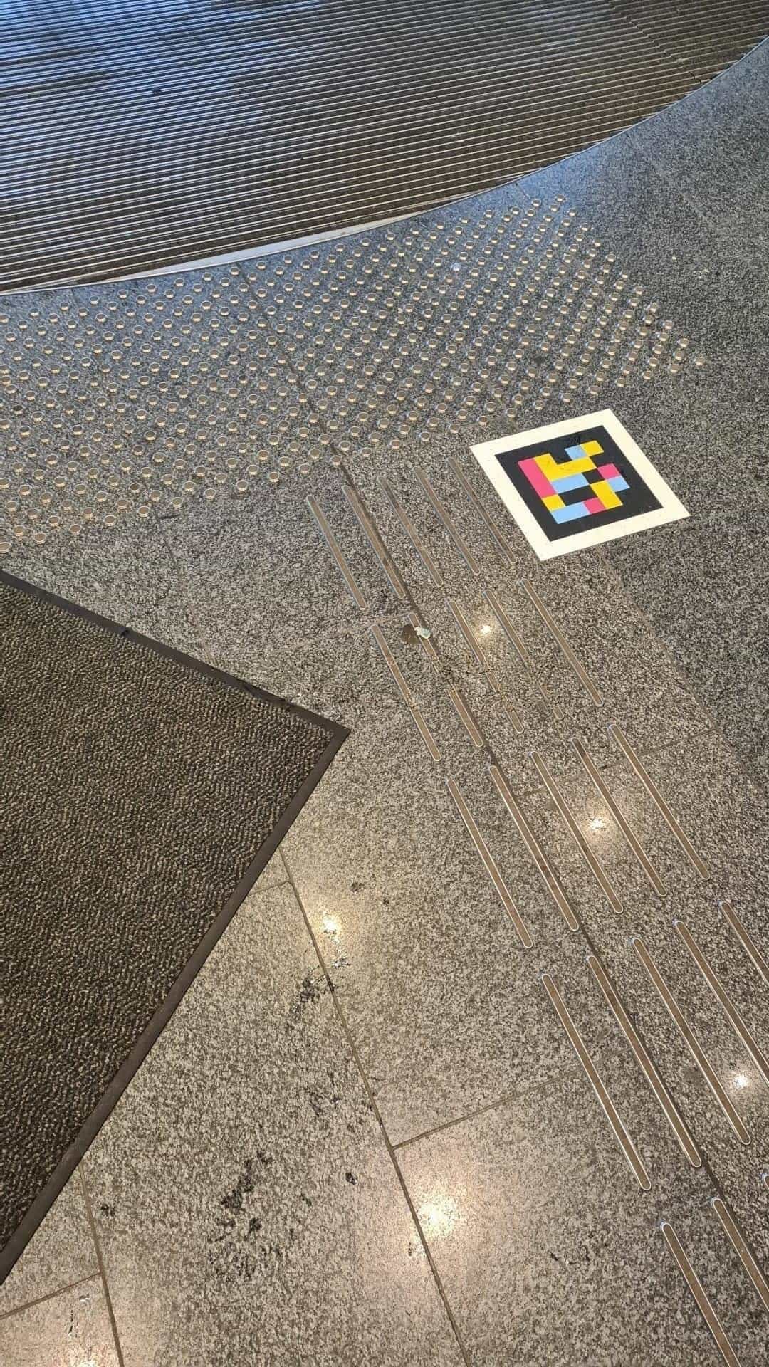 Detail of the polished grey granite floor inside the Klett-Passage: metal guide lines embedded in the pavement lead to a NaviLens code next to a tactile dotted area
